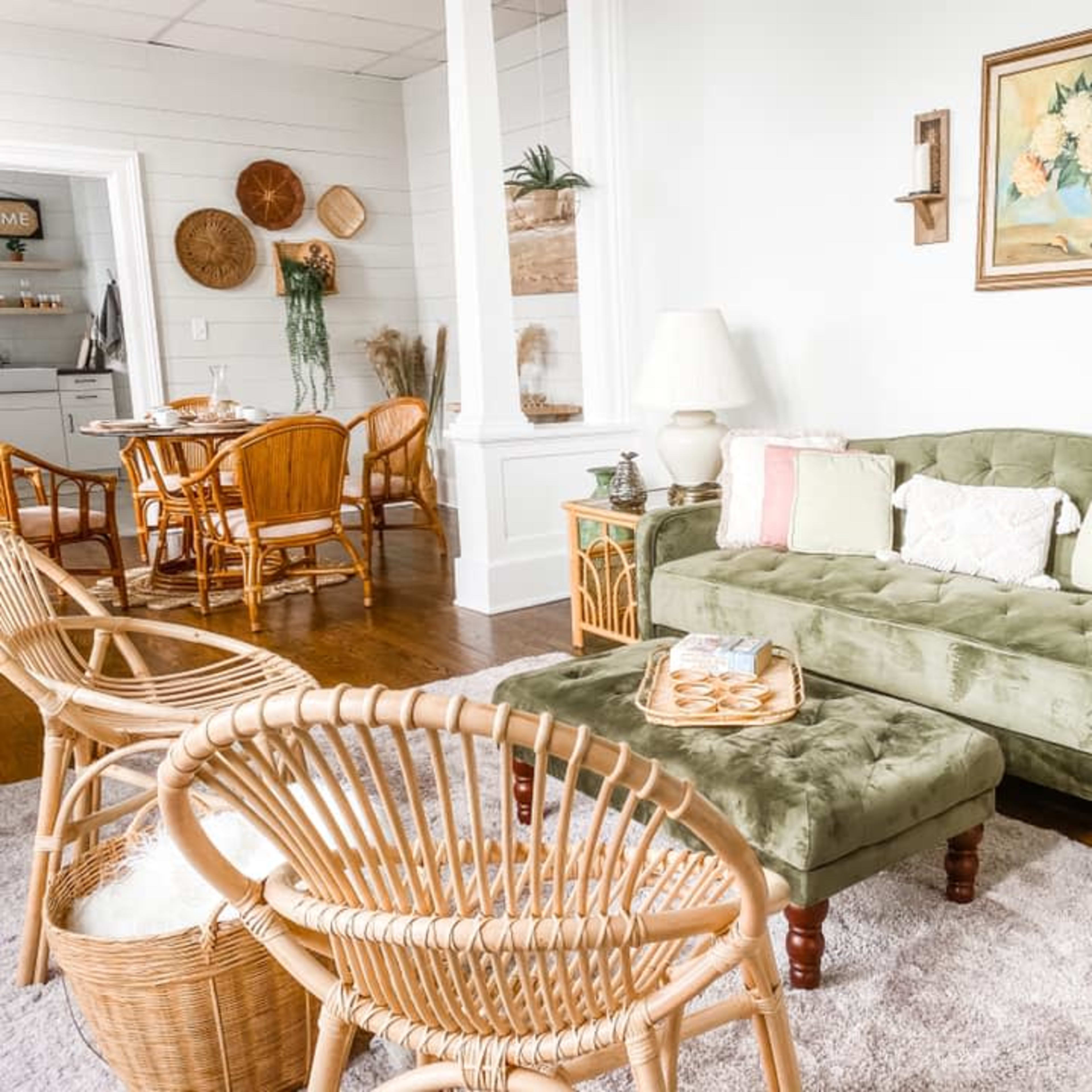 A cozy living room with a green sofa, wicker chairs, and a coffee table, arranged around a light-colored rug.