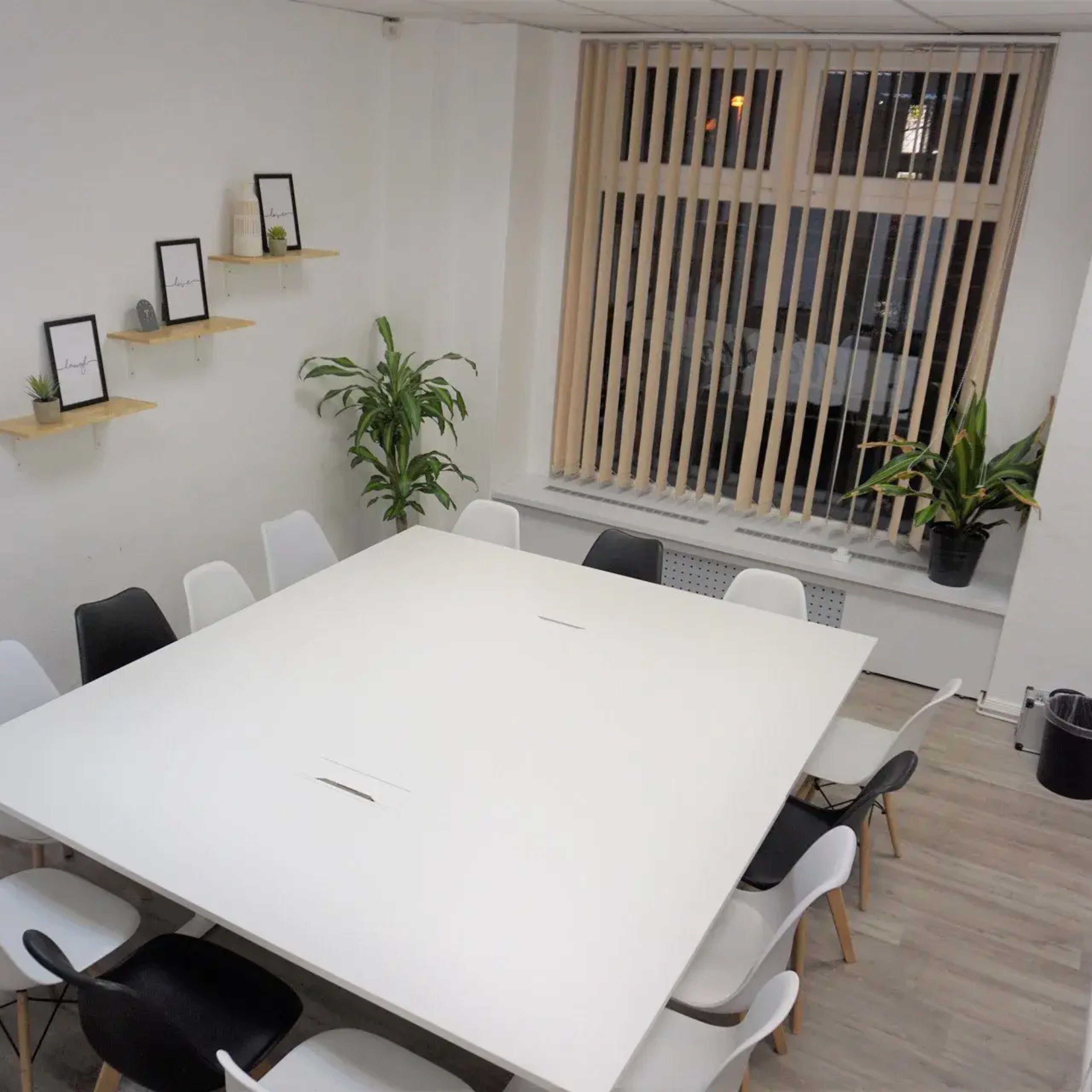 A spacious conference room features a large white table surrounded by chairs and is illuminated by natural light from a window.
