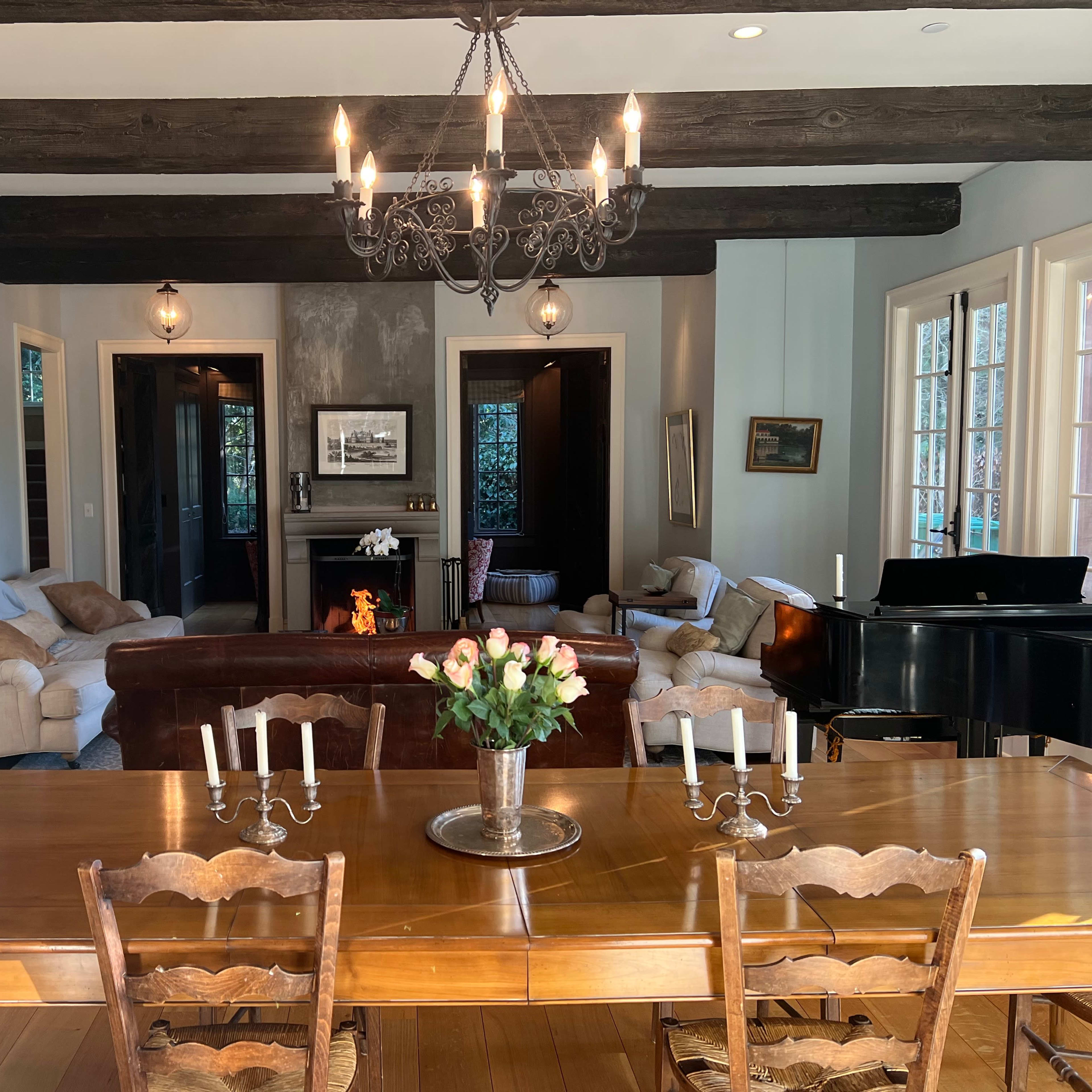 A spacious living area features a dining table with candles in the foreground, while a piano and comfortable seating are visible in the background.