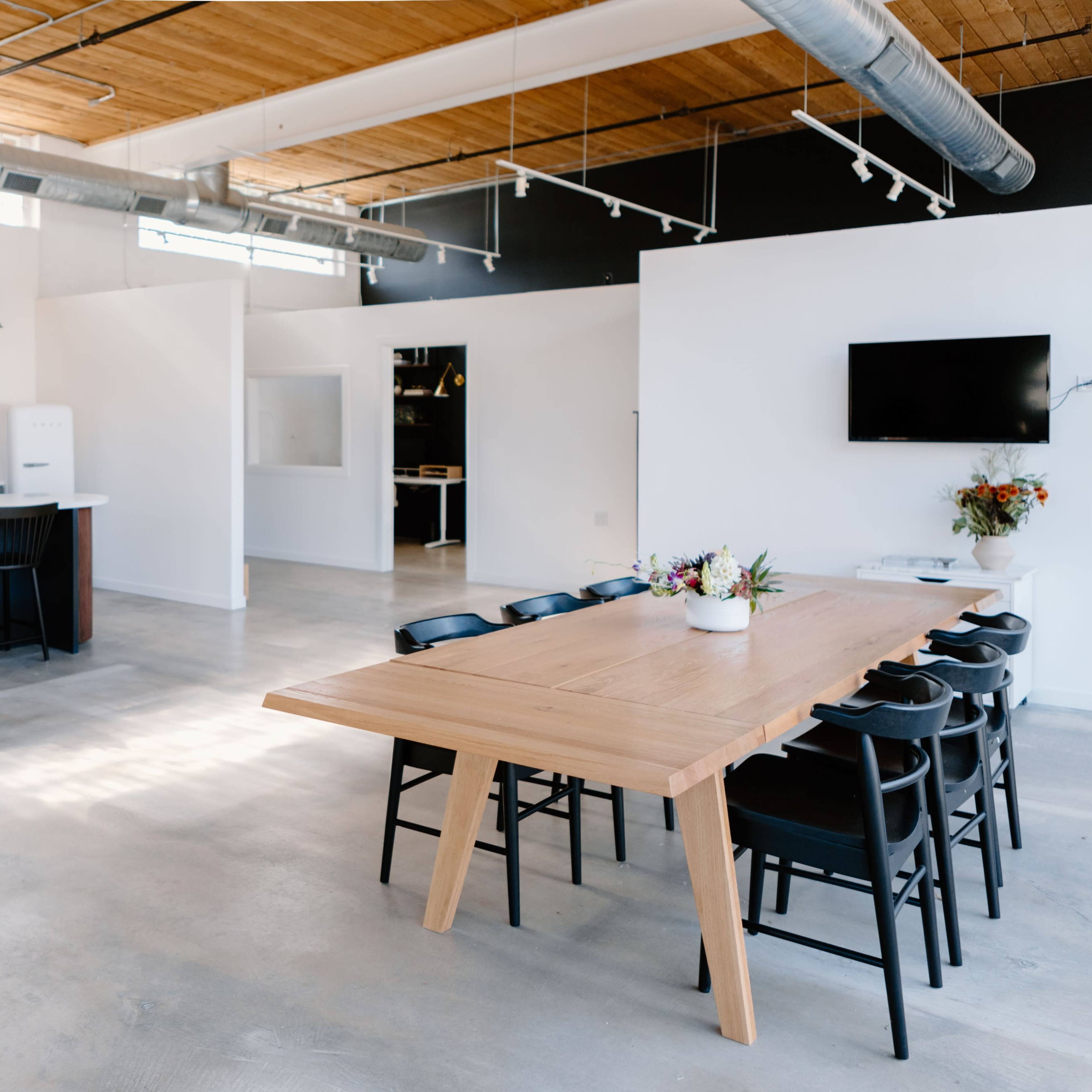 A modern kitchen and dining area features an open layout with a large wooden table, black chairs, and a well-equipped kitchen.