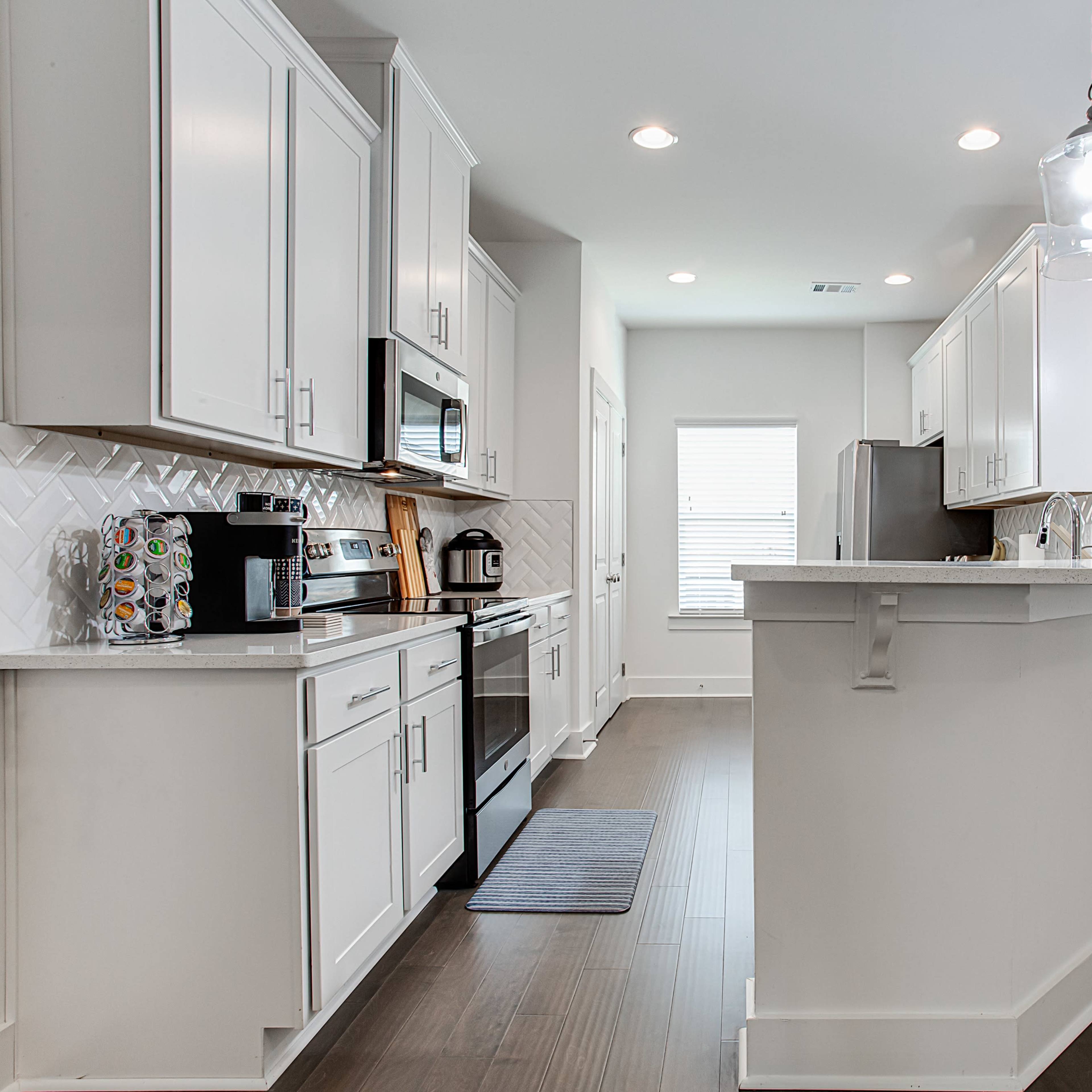 A modern kitchen with white cabinets, stainless steel appliances, and an island bar with stools, adjacent to a dining area.