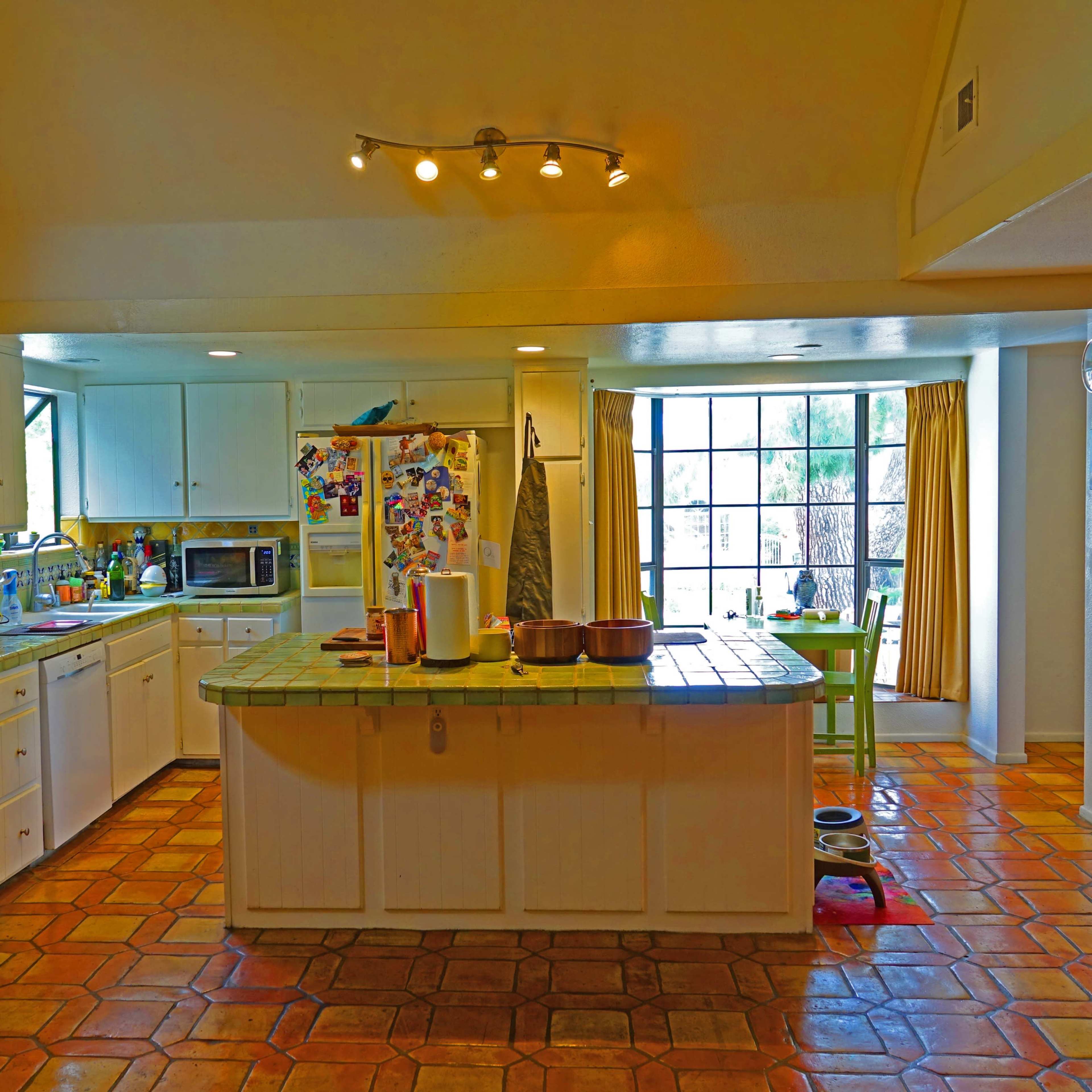 The kitchen features white cabinetry, a tiled island in the center, and a large window with natural light illuminating the space.