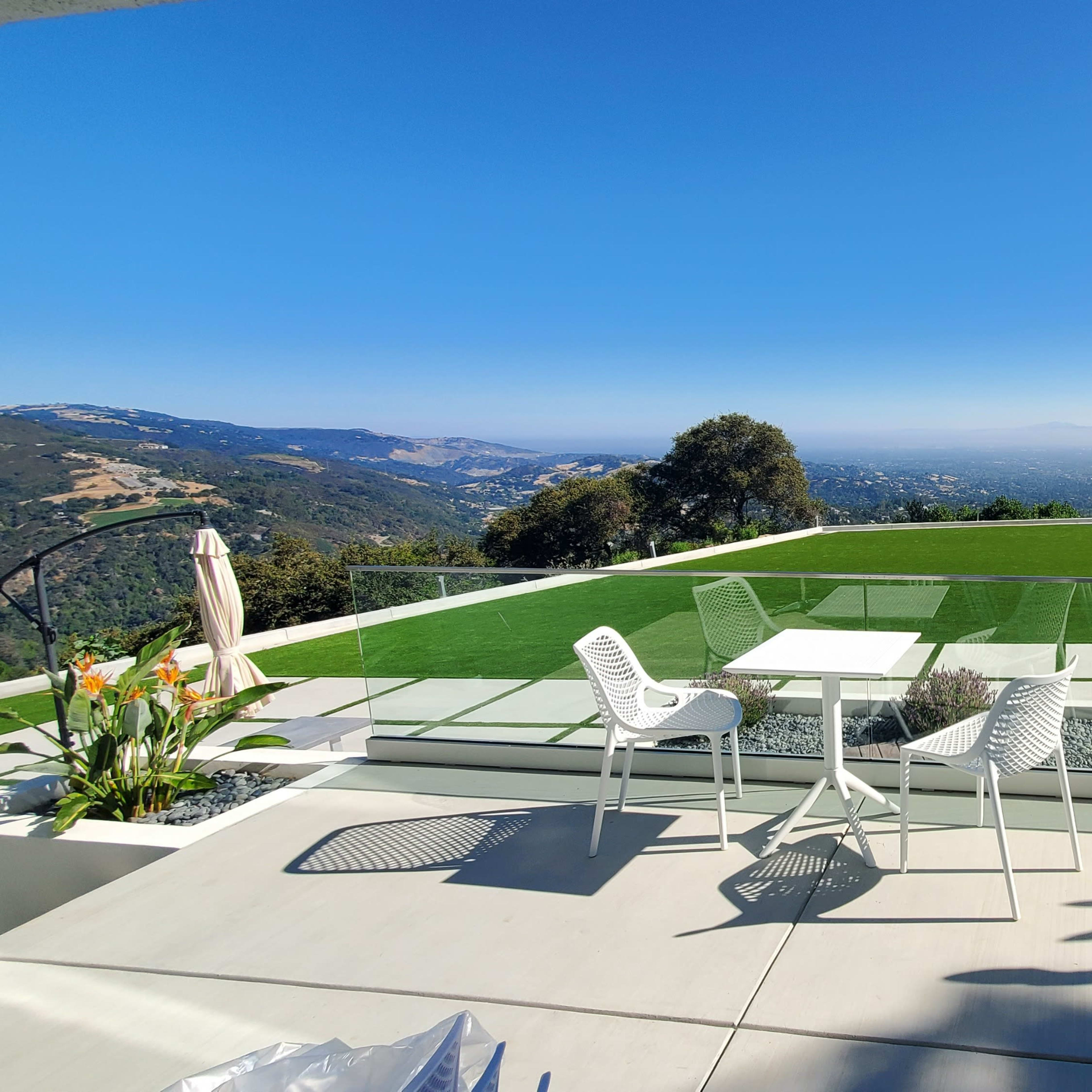 A modern patio overlooking a green lawn and a panoramic view of distant hills under a clear blue sky.