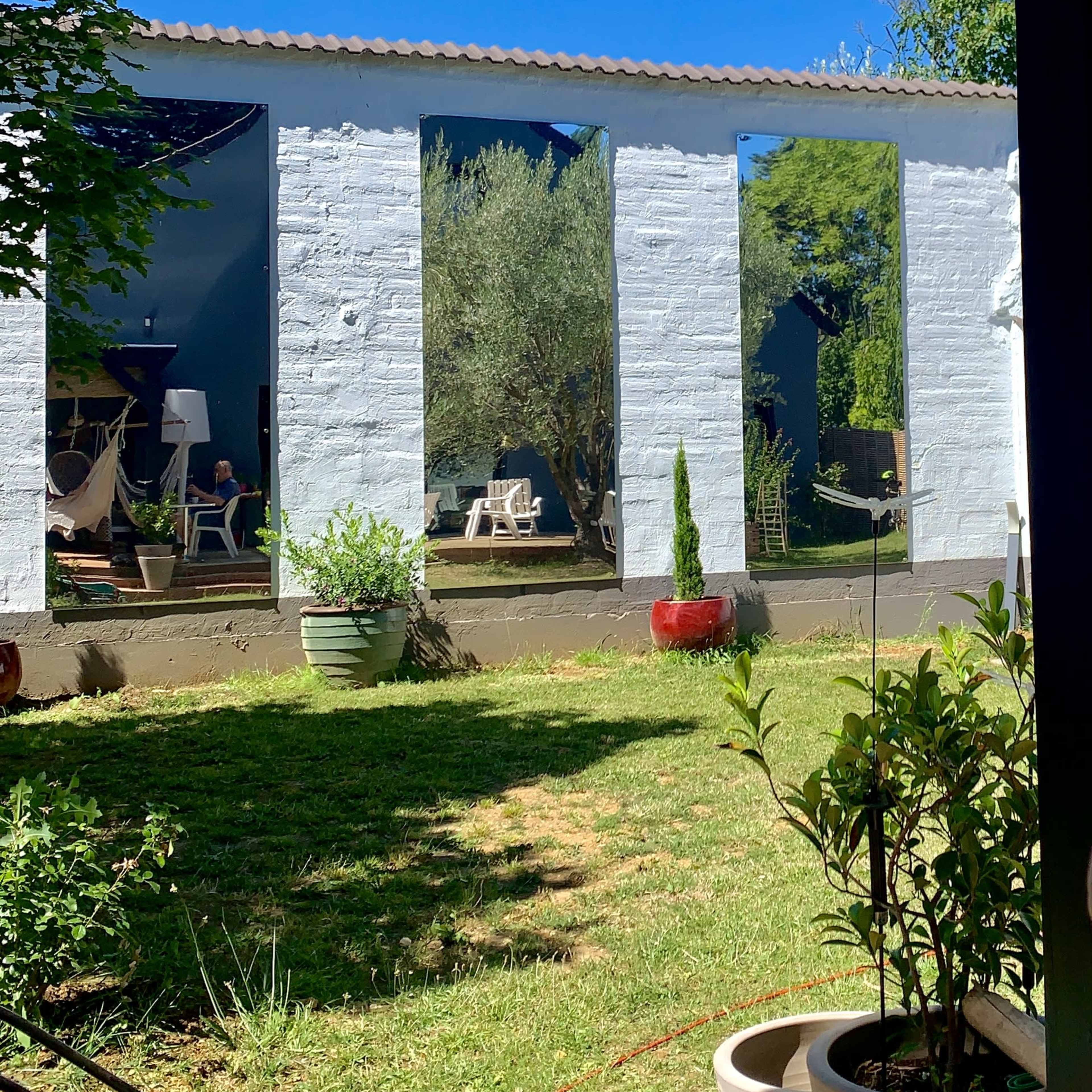 A white-walled building with large openings, surrounded by greenery and potted plants under a clear blue sky.