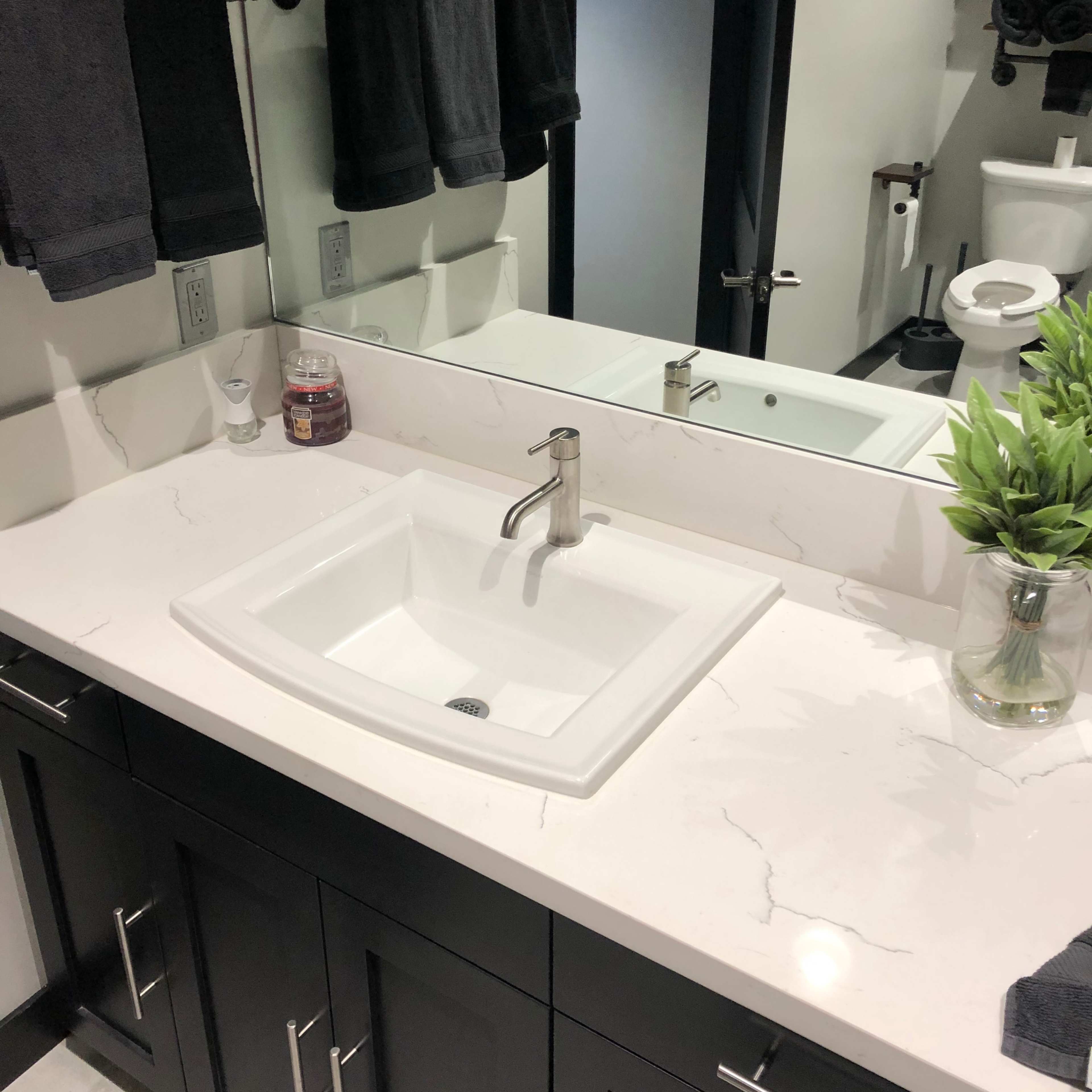 A modern bathroom sink area featuring a white sink, dark cabinetry, a mirror, and neatly arranged towels.