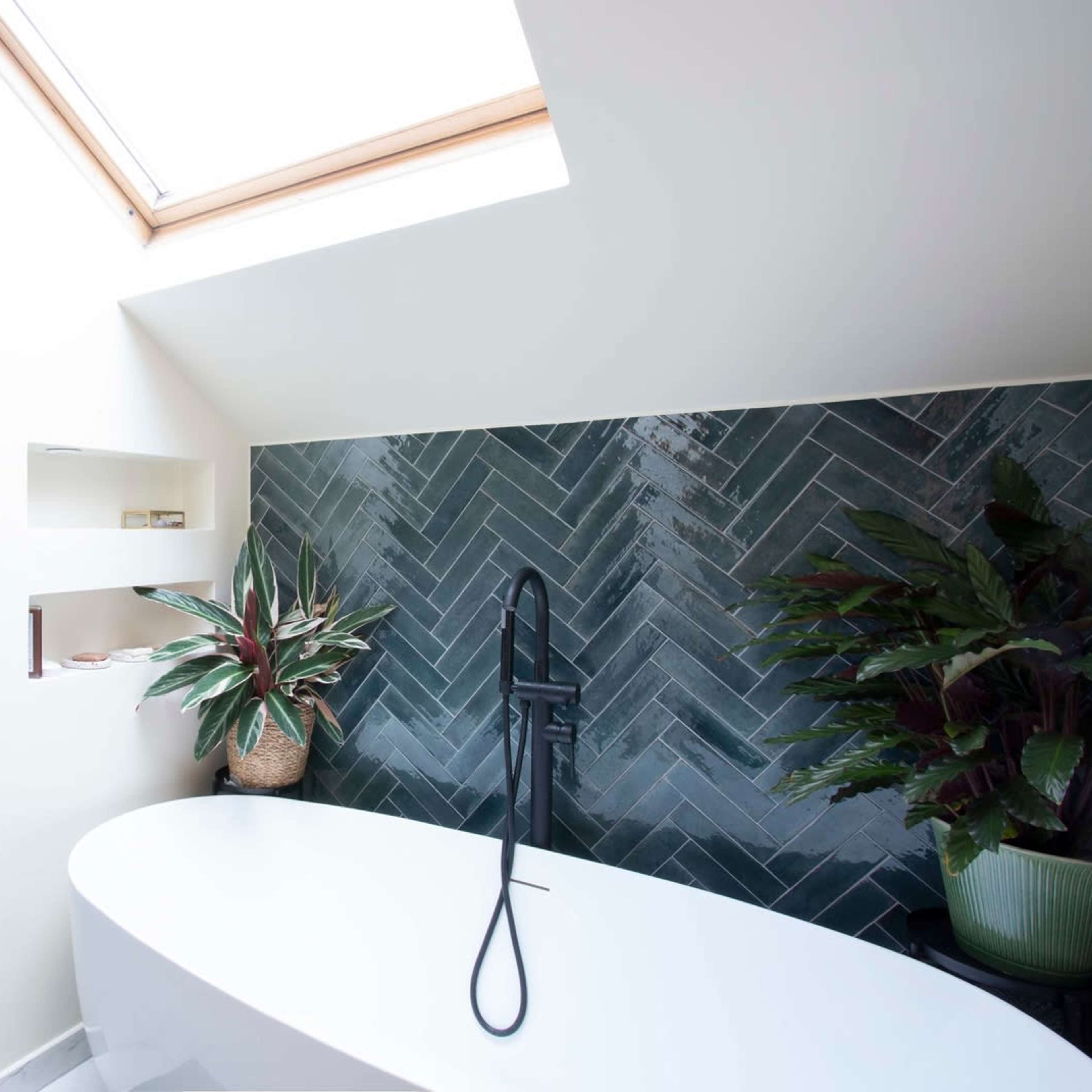 A modern bathroom with a freestanding bathtub, a green herringbone tile accent wall, and a skylight allowing natural light to enter.