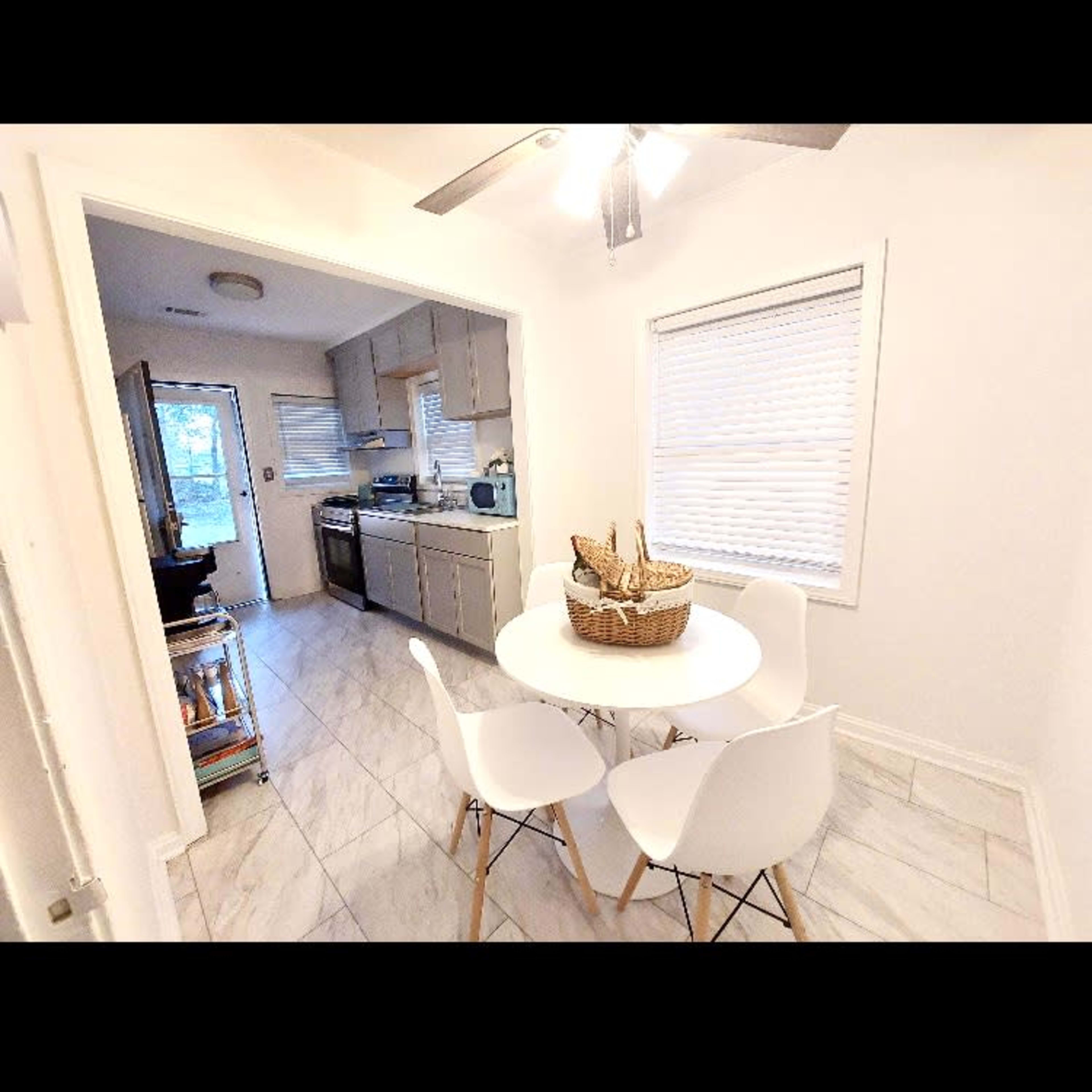 A small dining area features a round white table surrounded by four chairs, with a kitchen visible in the background.