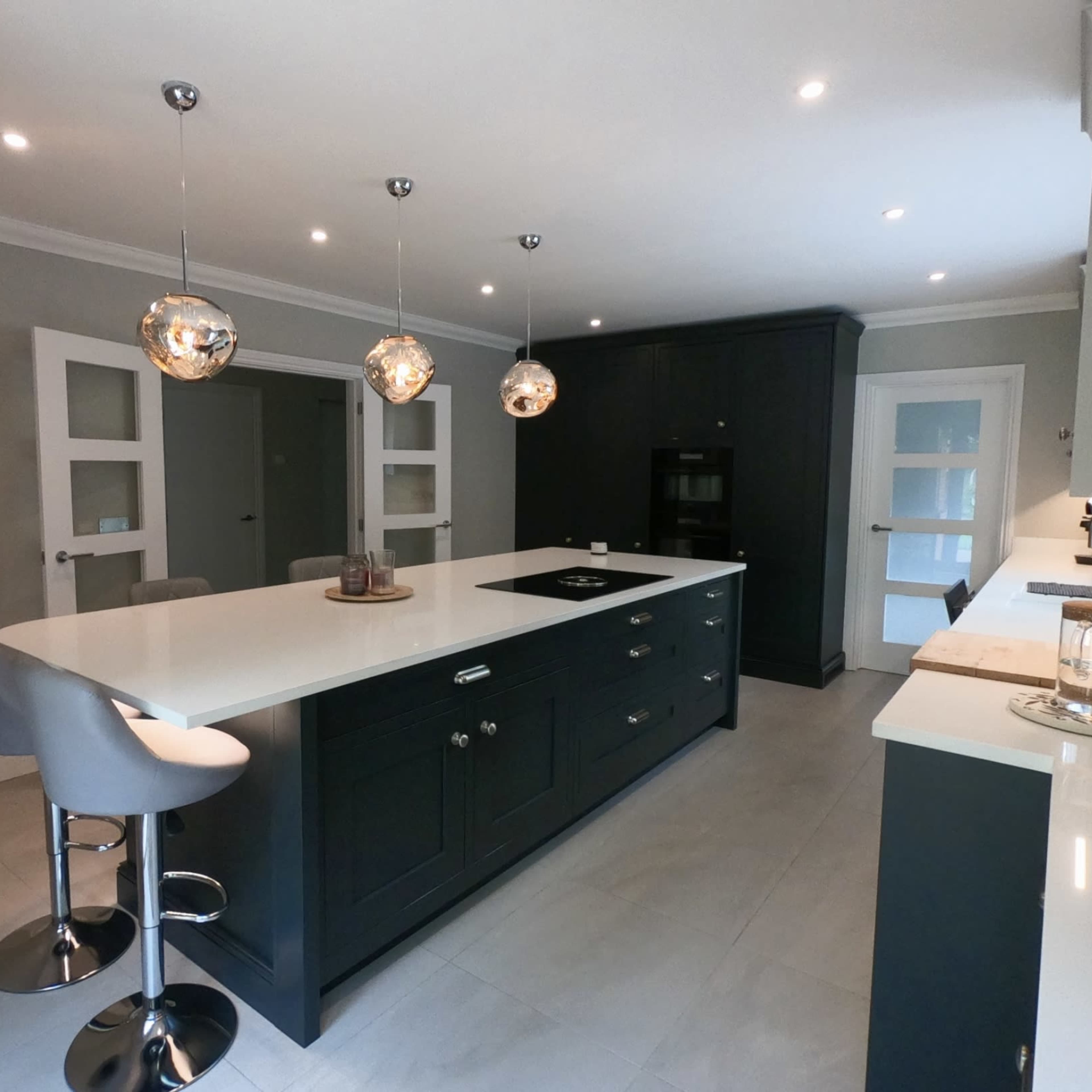 A modern kitchen features a central island with bar stools, pendant lighting, and a sleek design in grey and black tones.
