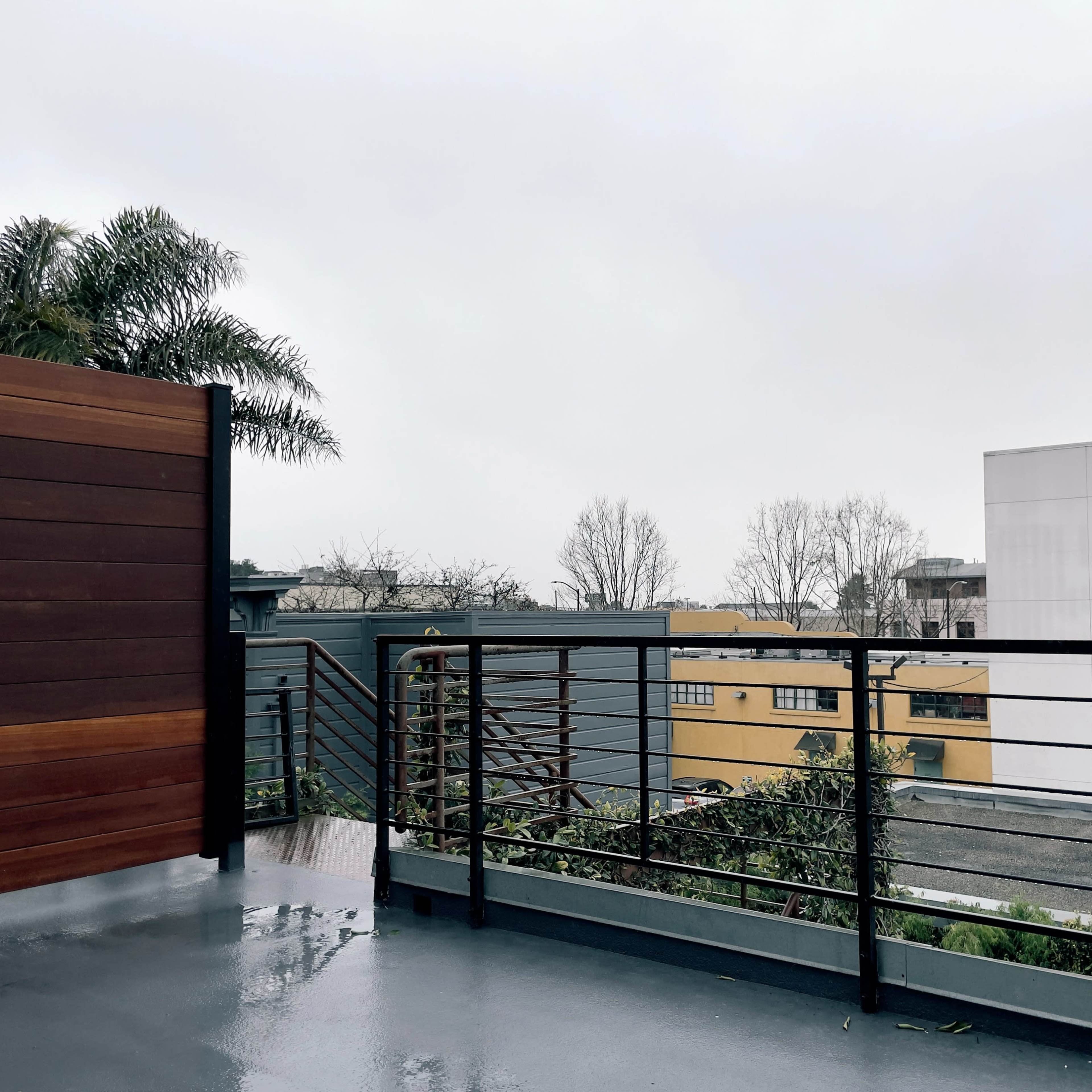 A balcony with wooden panels and metal railings overlooking an urban landscape in cloudy weather.