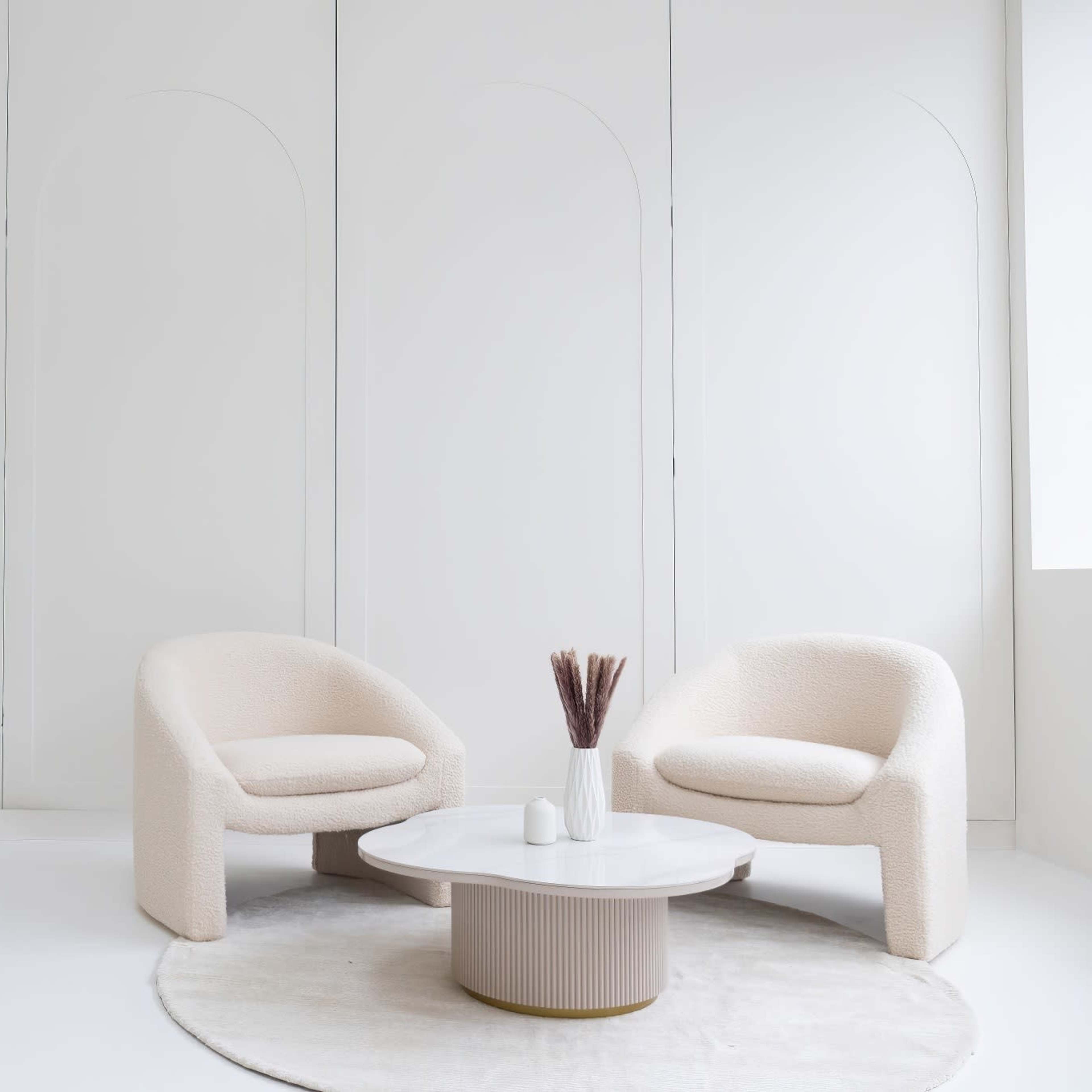 Two textured beige chairs facing a round white coffee table on a circular rug in a minimalist, bright room with white walls.