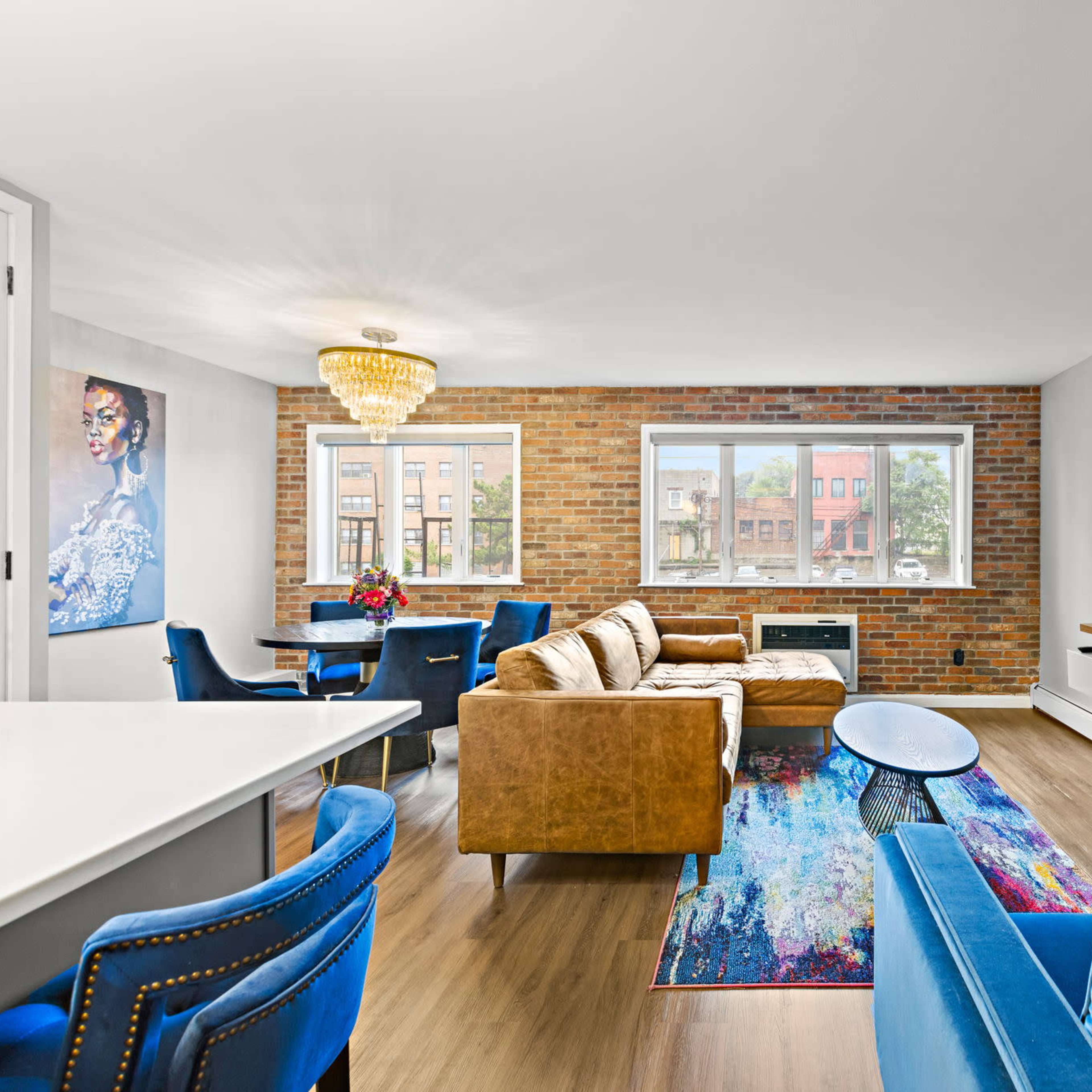 A modern living room features a seating area with brown and blue couches, a large TV mounted on a wooden wall unit, and a dining space with blue chairs and a table.