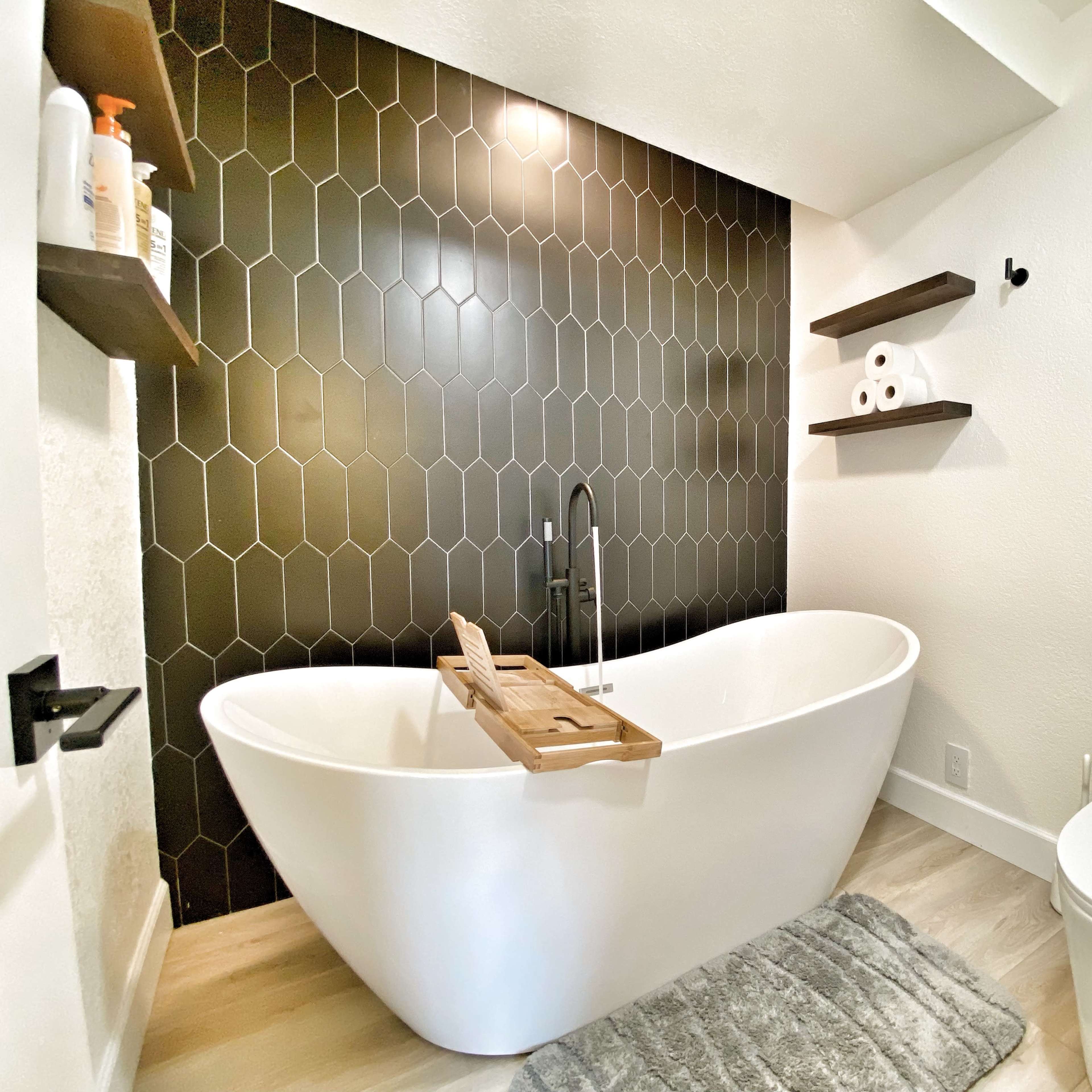 A modern bathroom features a freestanding white bathtub, a sleek toilet, and a dark hexagonal tiled accent wall.
