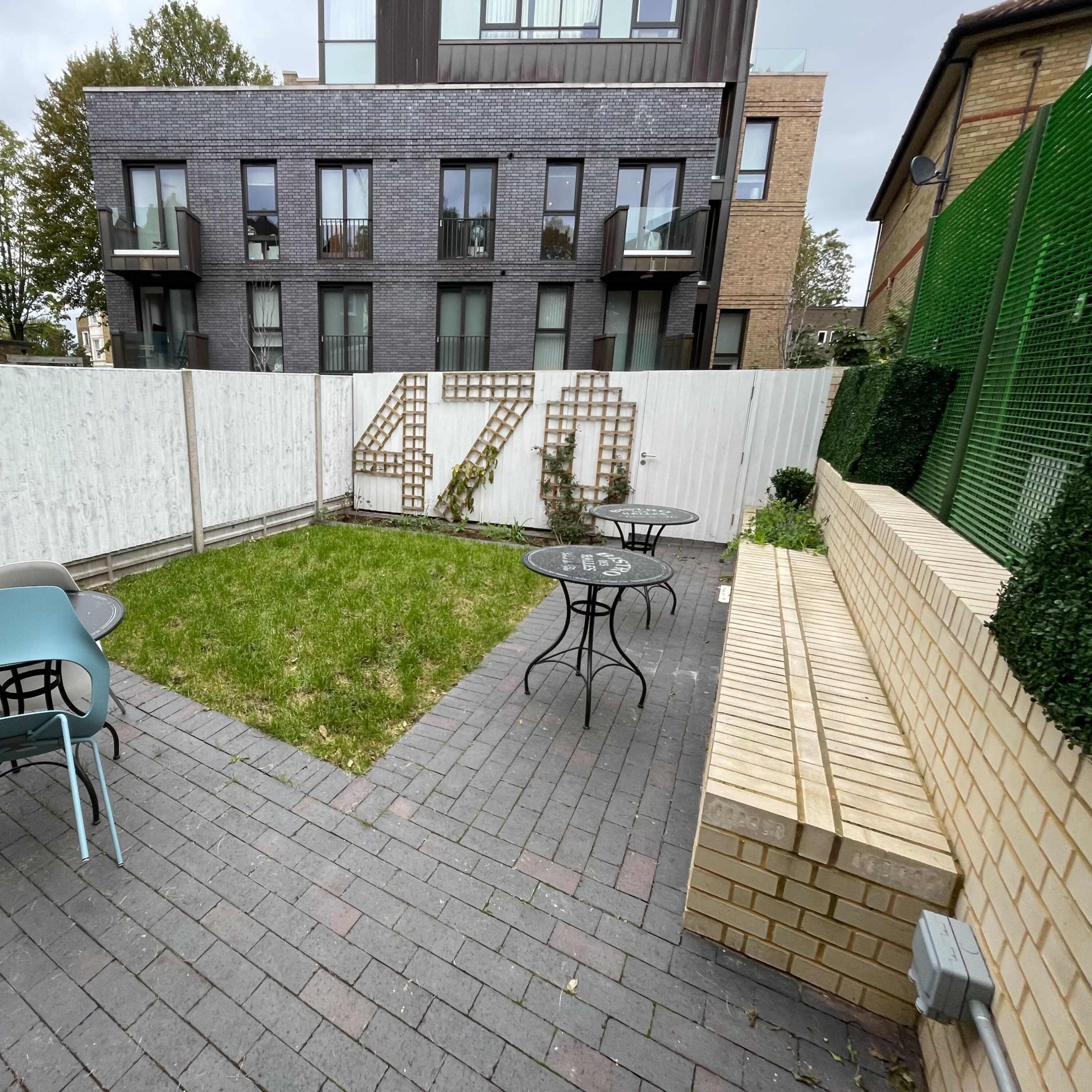 A small courtyard with green grass, several tables and chairs, and a white fence displaying the number "470."
