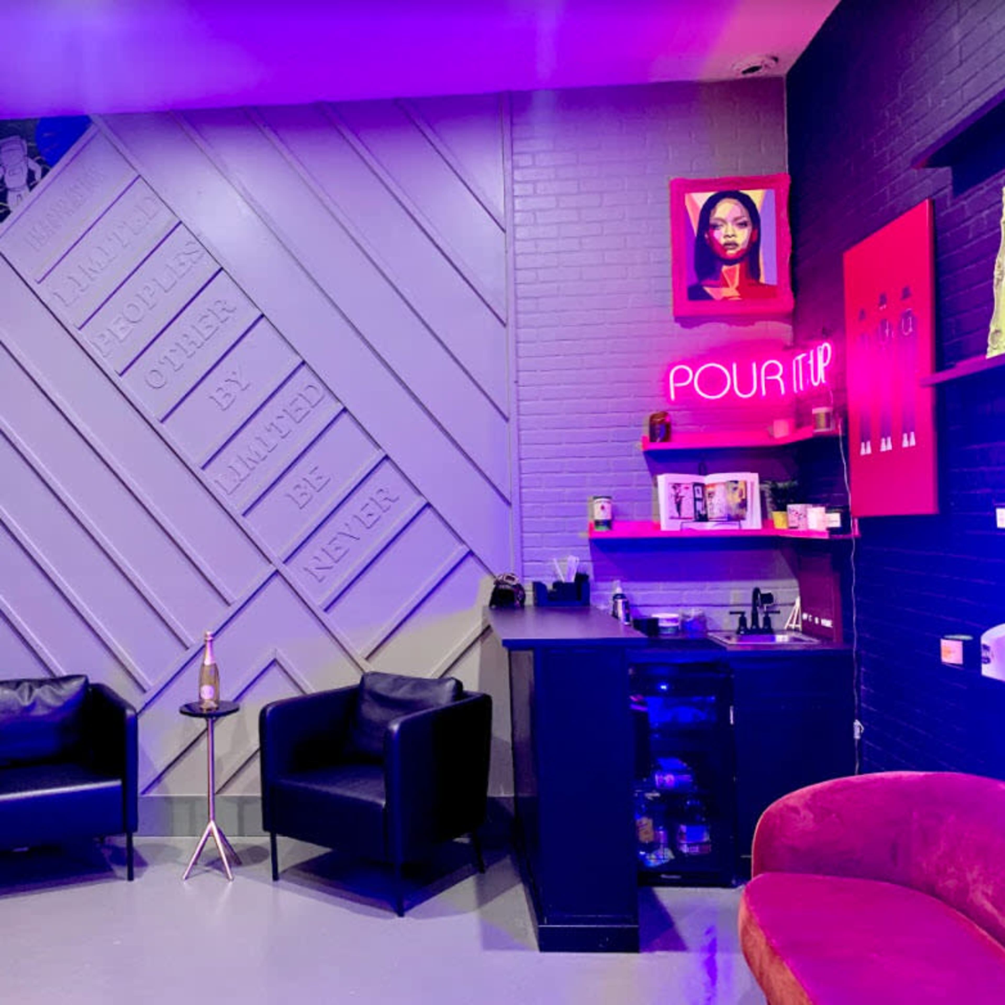 A modern interior of a lounge area with black chairs, a neon sign, and a wall adorned with framed artworks and greenery.