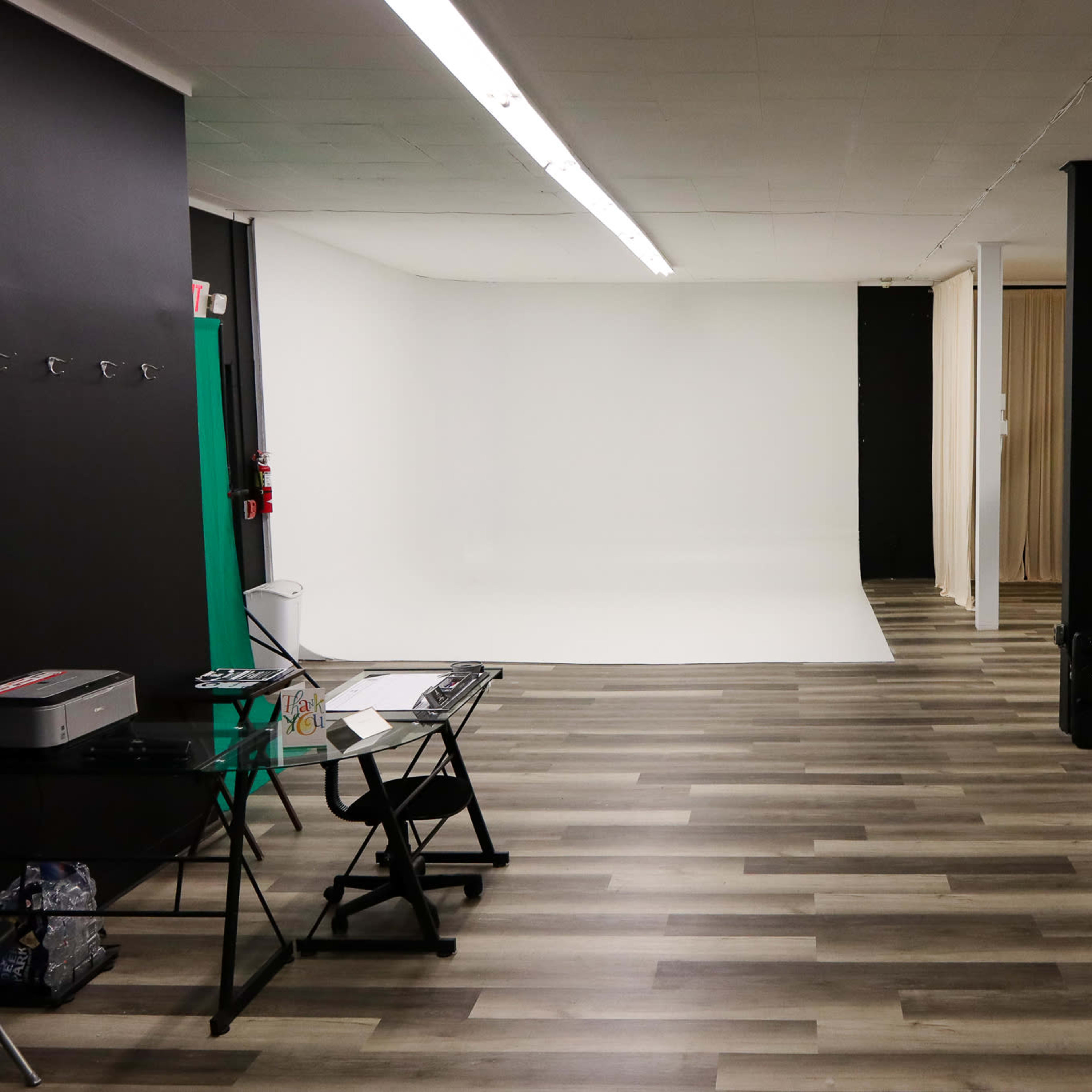 A spacious studio or gallery with a white backdrop on one side, wooden flooring, and various partitions and equipment visible.
