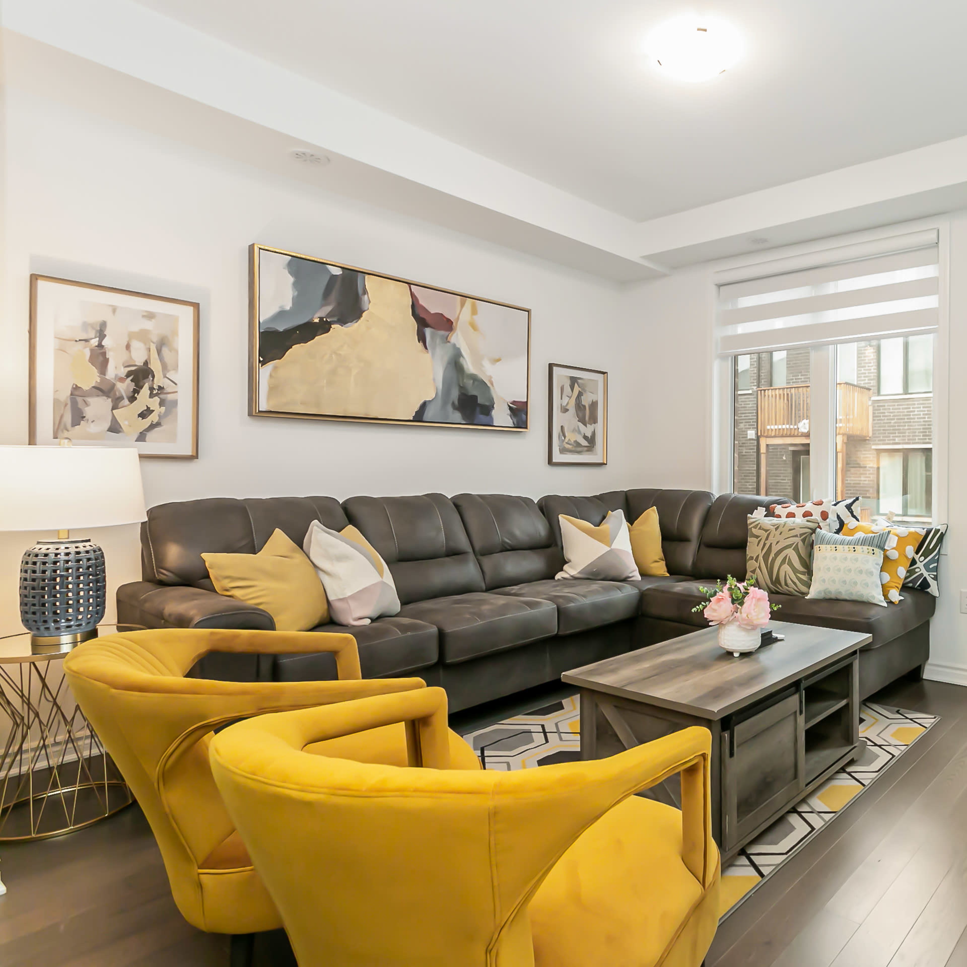 The living room features a large sectional sofa, two yellow chairs, a coffee table, and a door leading to a balcony.