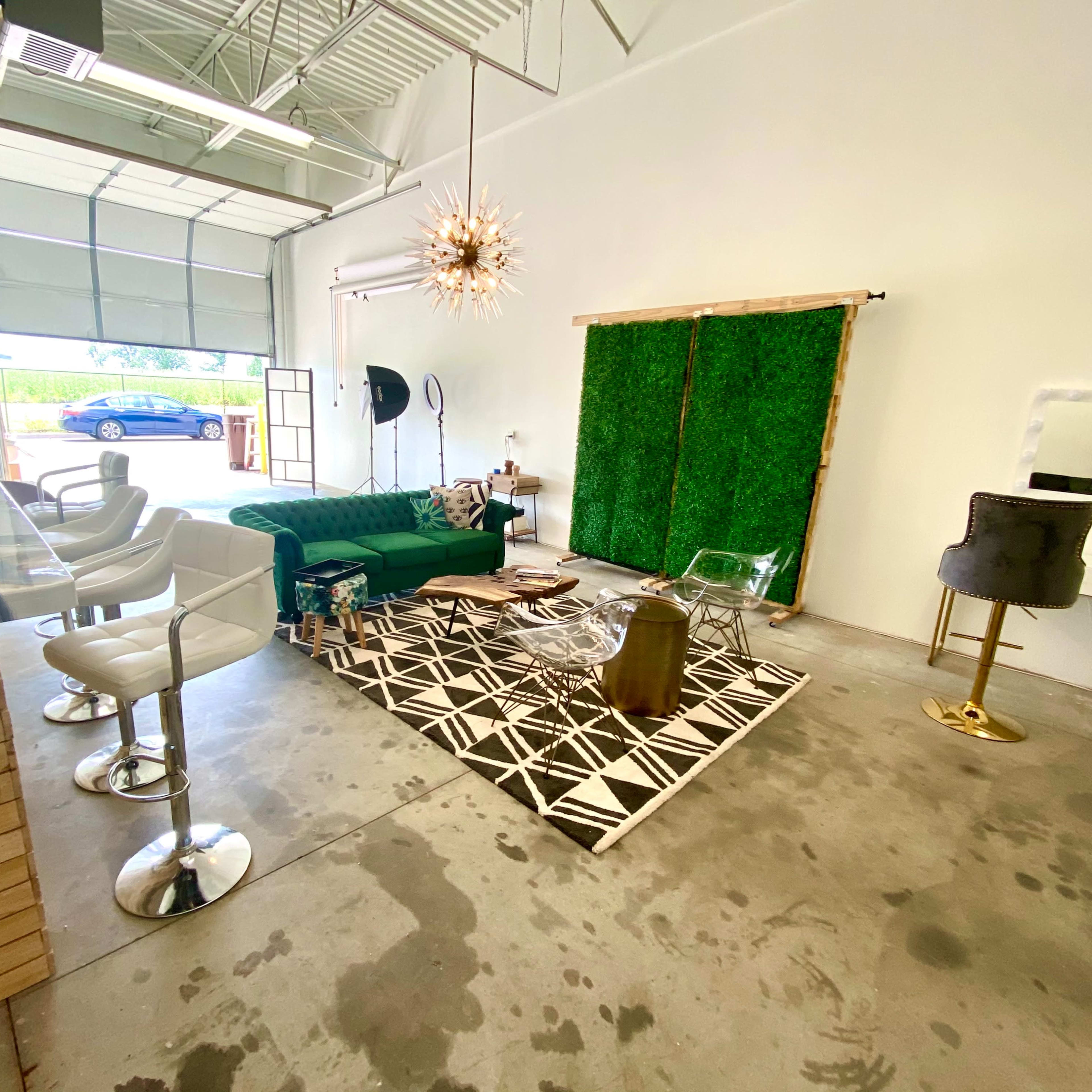 A modern interior space with a green sofa, a geometric rug, a lounge area with clear chairs, and a decorative wall made of greenery.