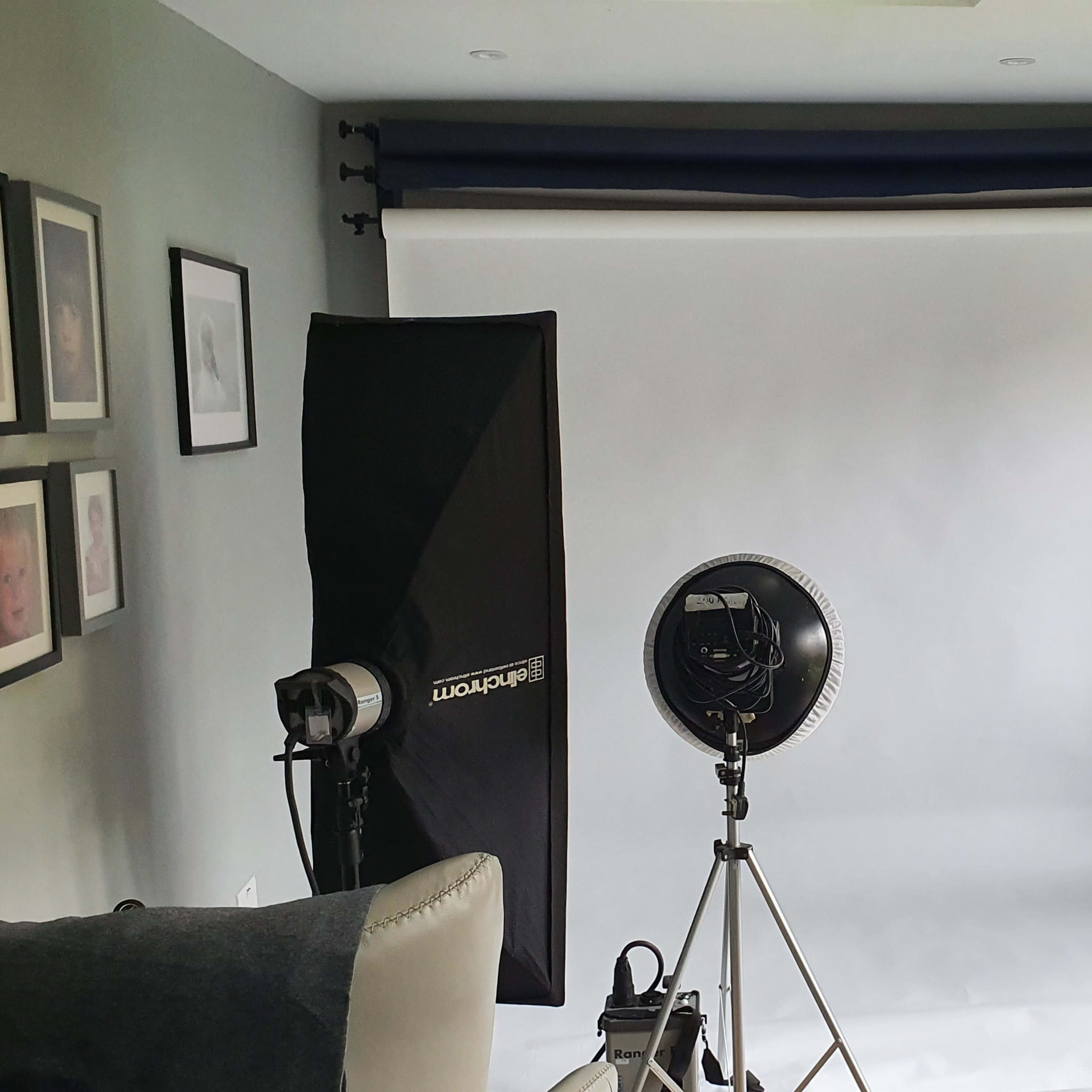 A photo studio setup with two softbox lights and a circular light on stands, facing a white backdrop.
