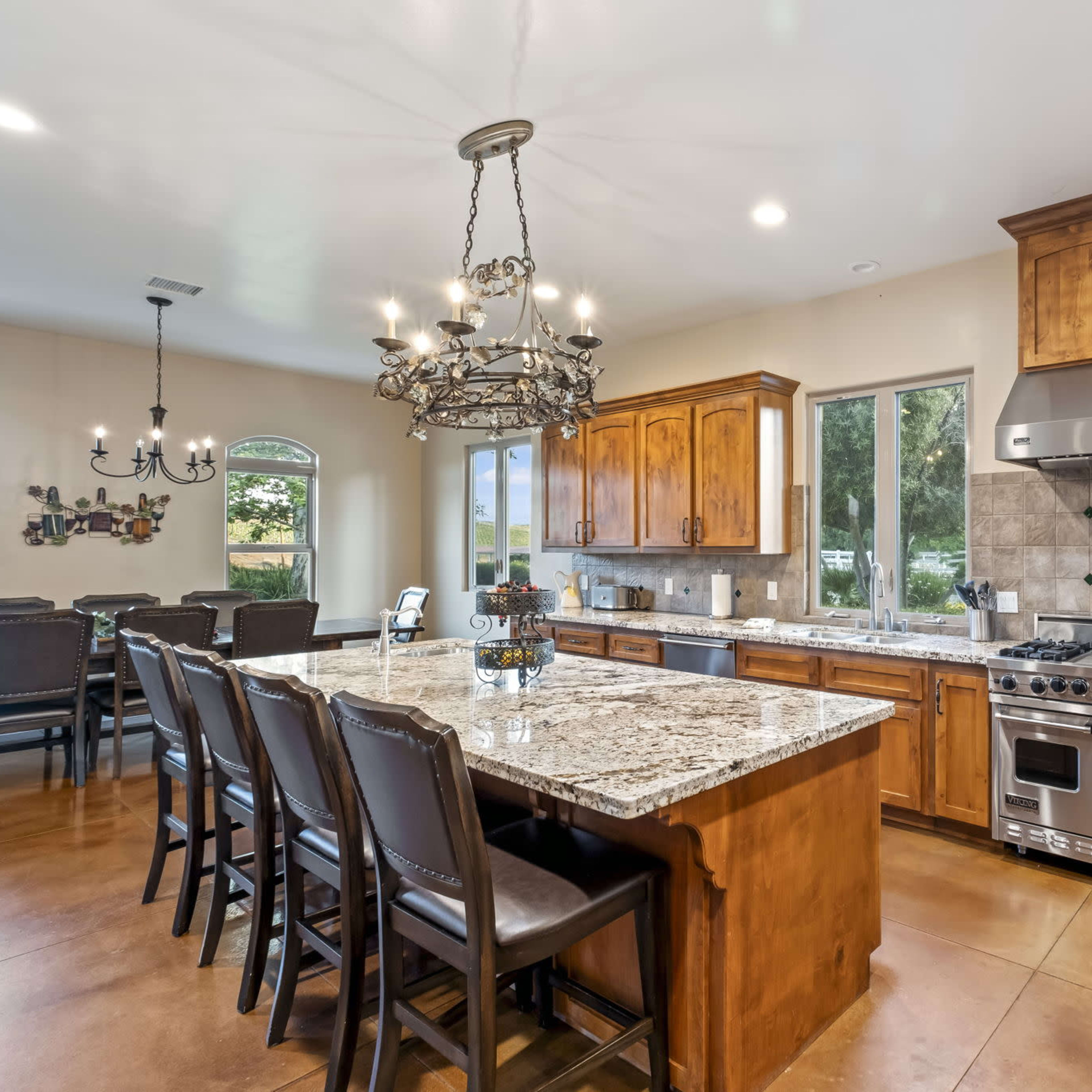 A spacious kitchen features wooden cabinetry, a large granite island with seating, and stainless steel appliances.