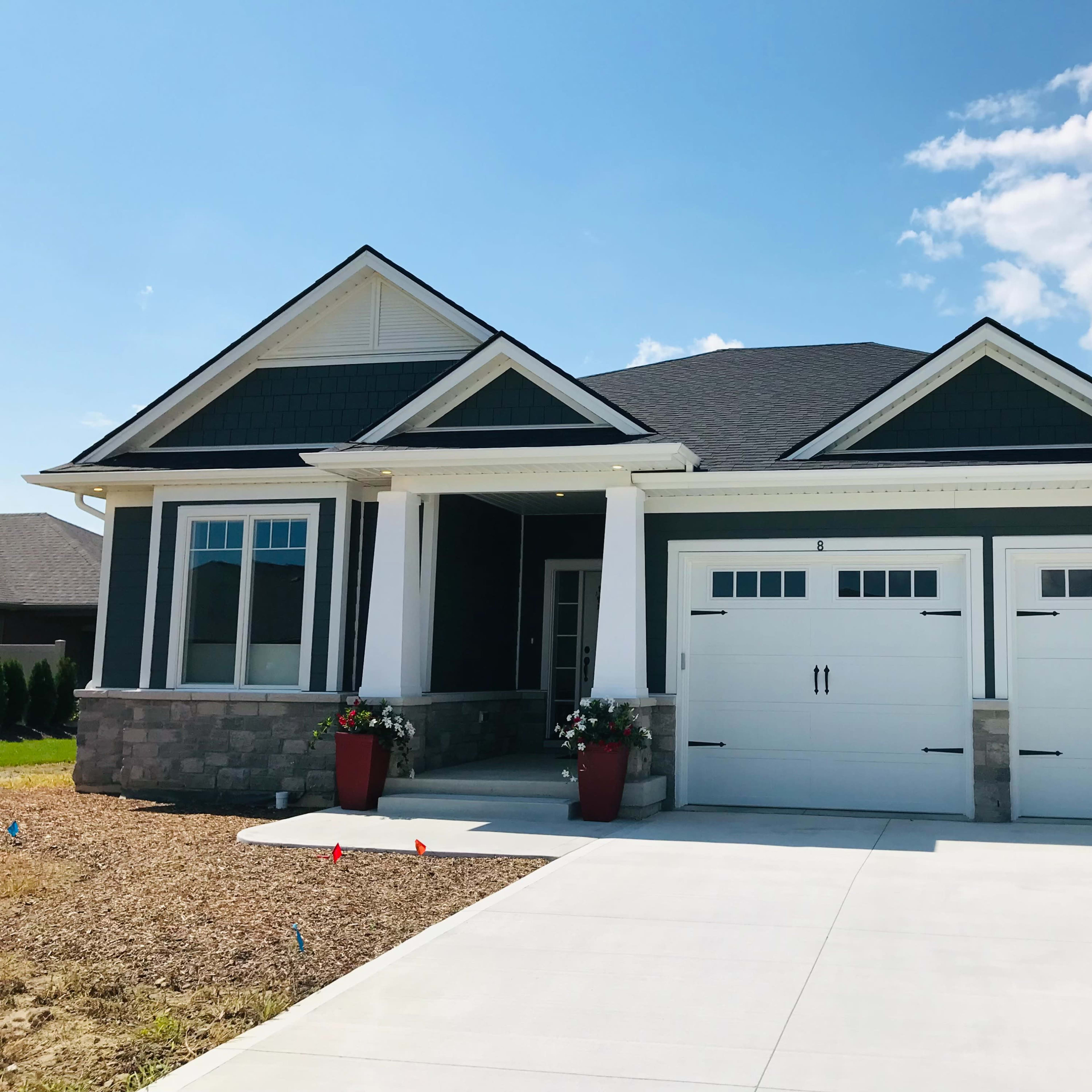 A single-story house with a dark exterior, two garage doors, and a front porch featuring planters.