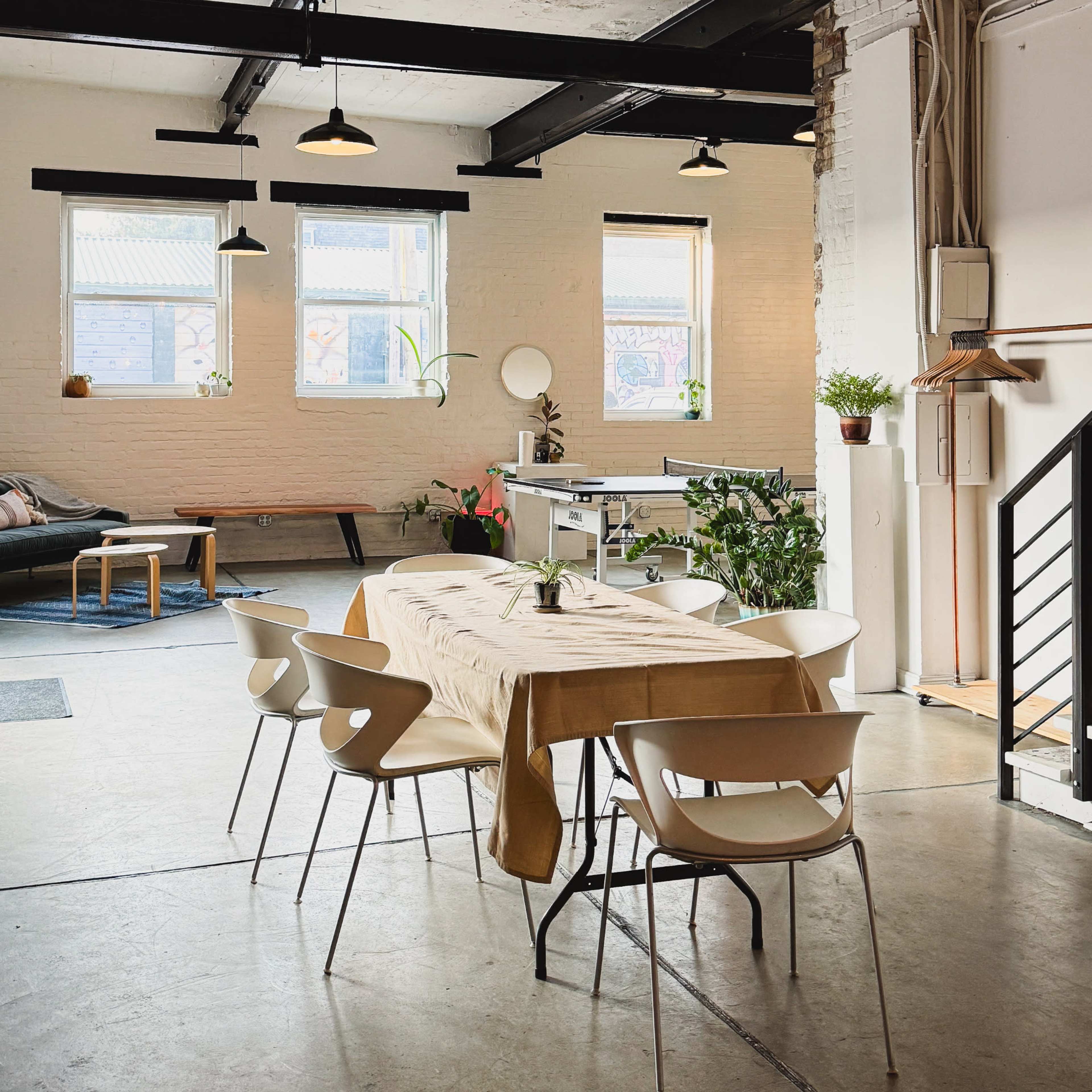 A spacious, modern interior with a dining table surrounded by white chairs, large windows, and exposed beams.