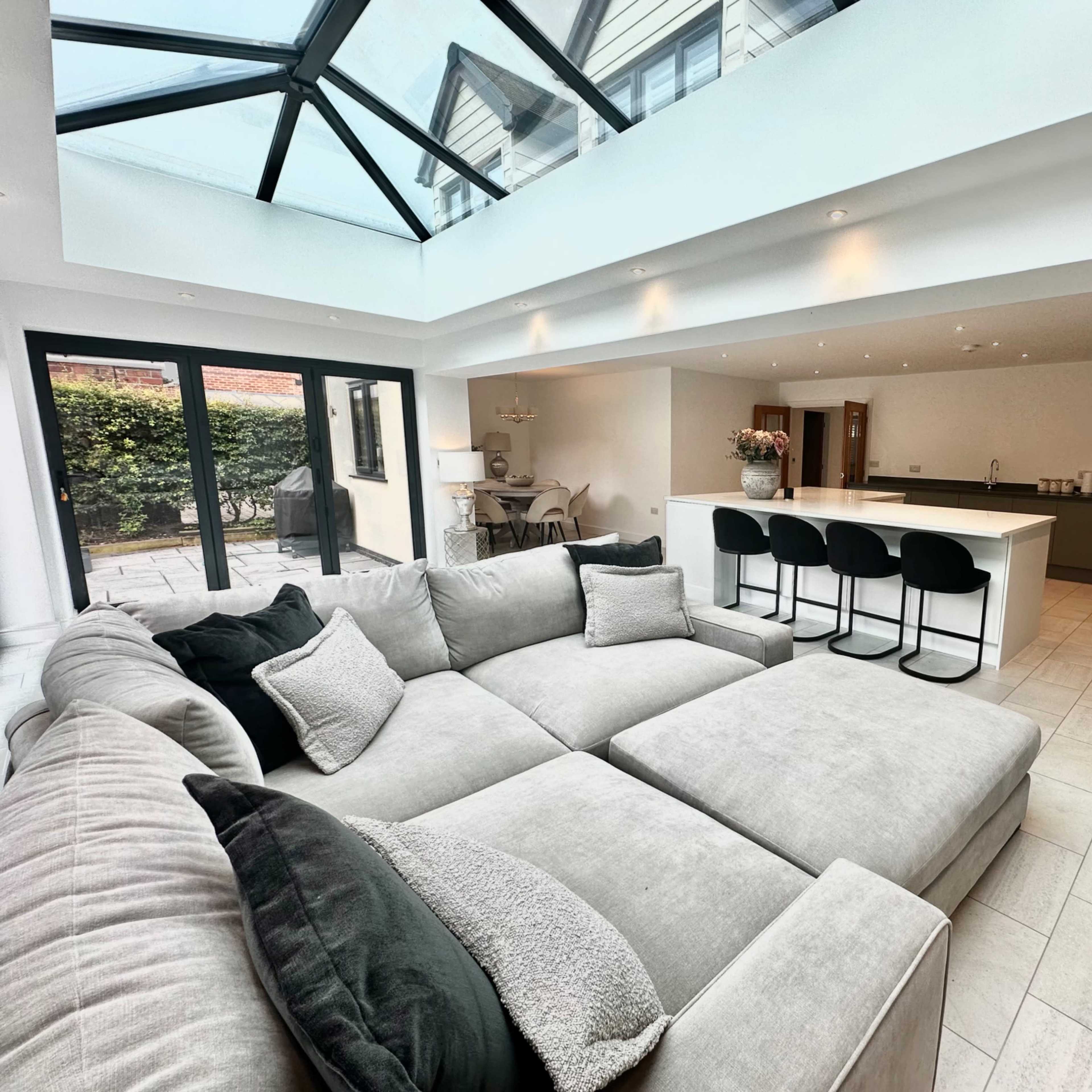A modern living space with a plush gray sectional sofa, a large island kitchen, and a glass ceiling that allows natural light to fill the area.