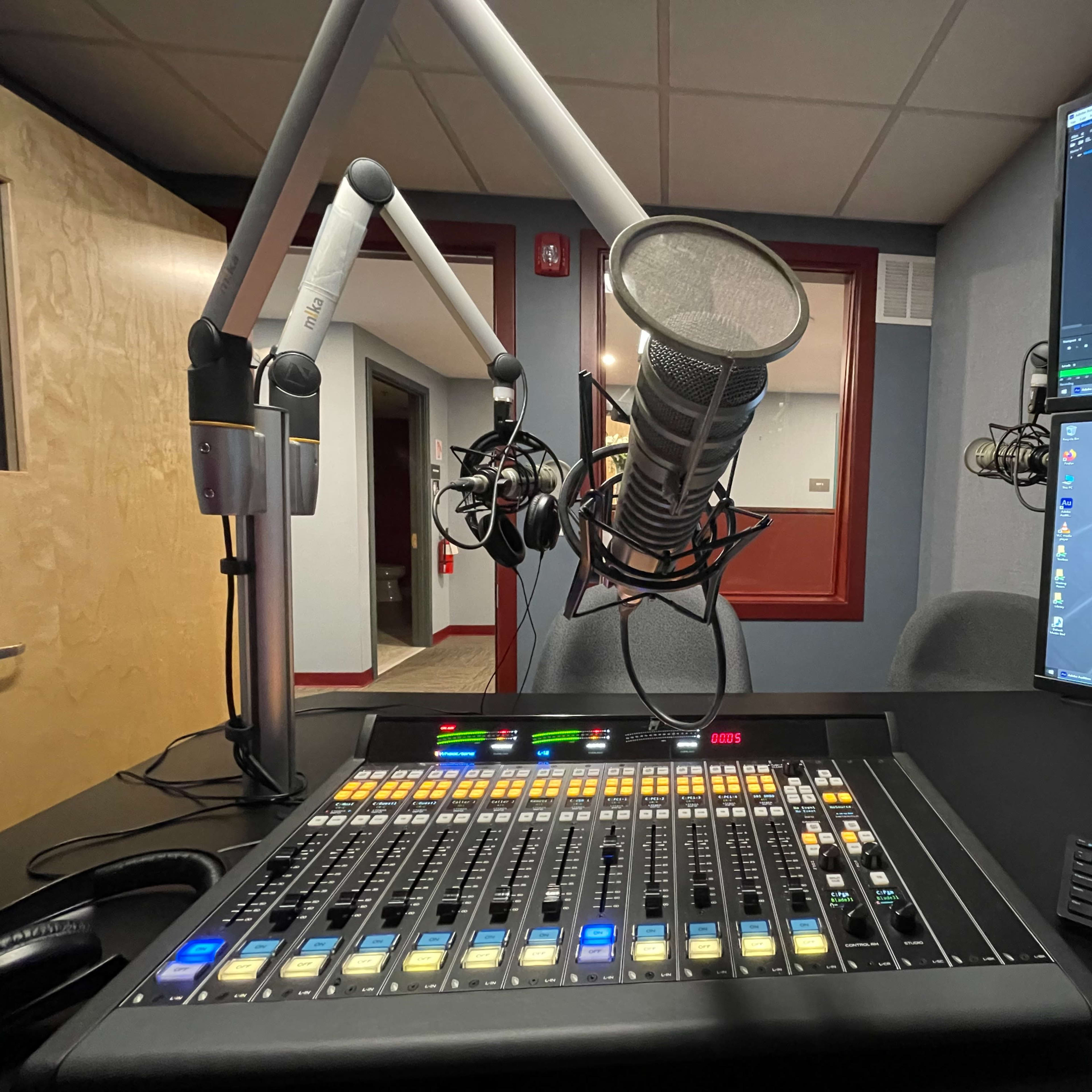 A radio studio setup with a microphone, mixing console, and computer monitors displaying sound waveforms.