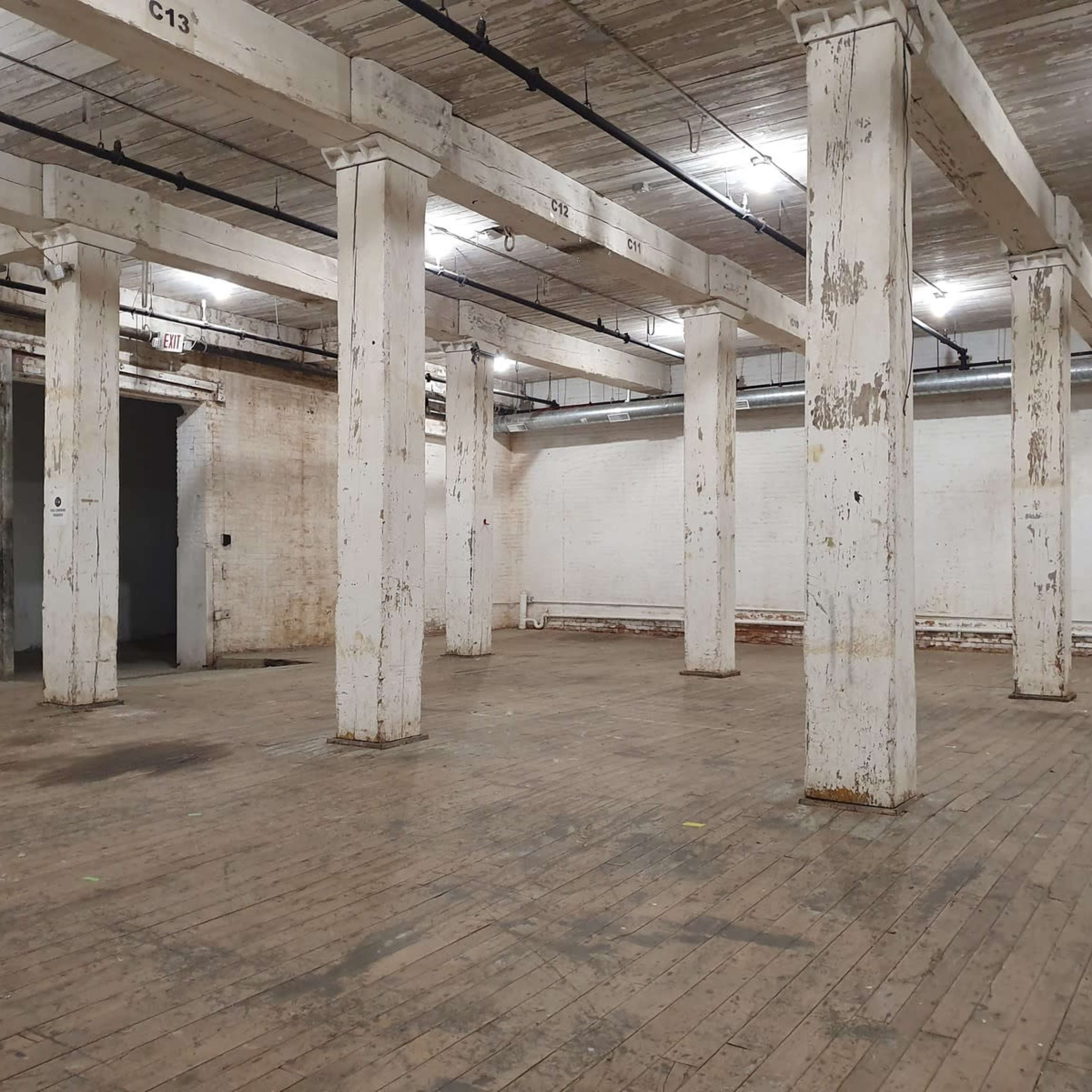 An empty industrial space with wooden floors and several large white columns.