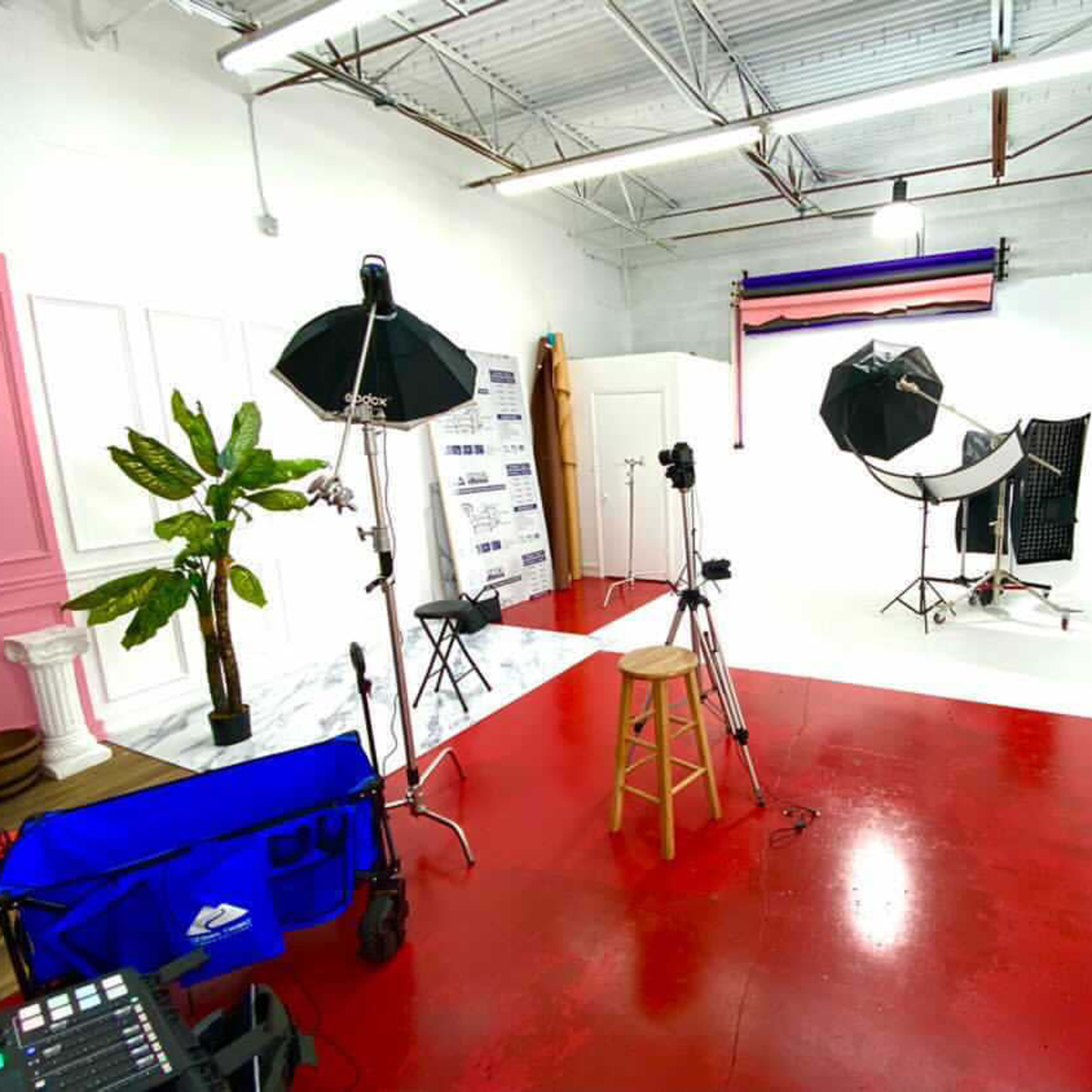 A photography studio with red flooring, various lighting equipment, a backdrop, and a few props arranged throughout the space.