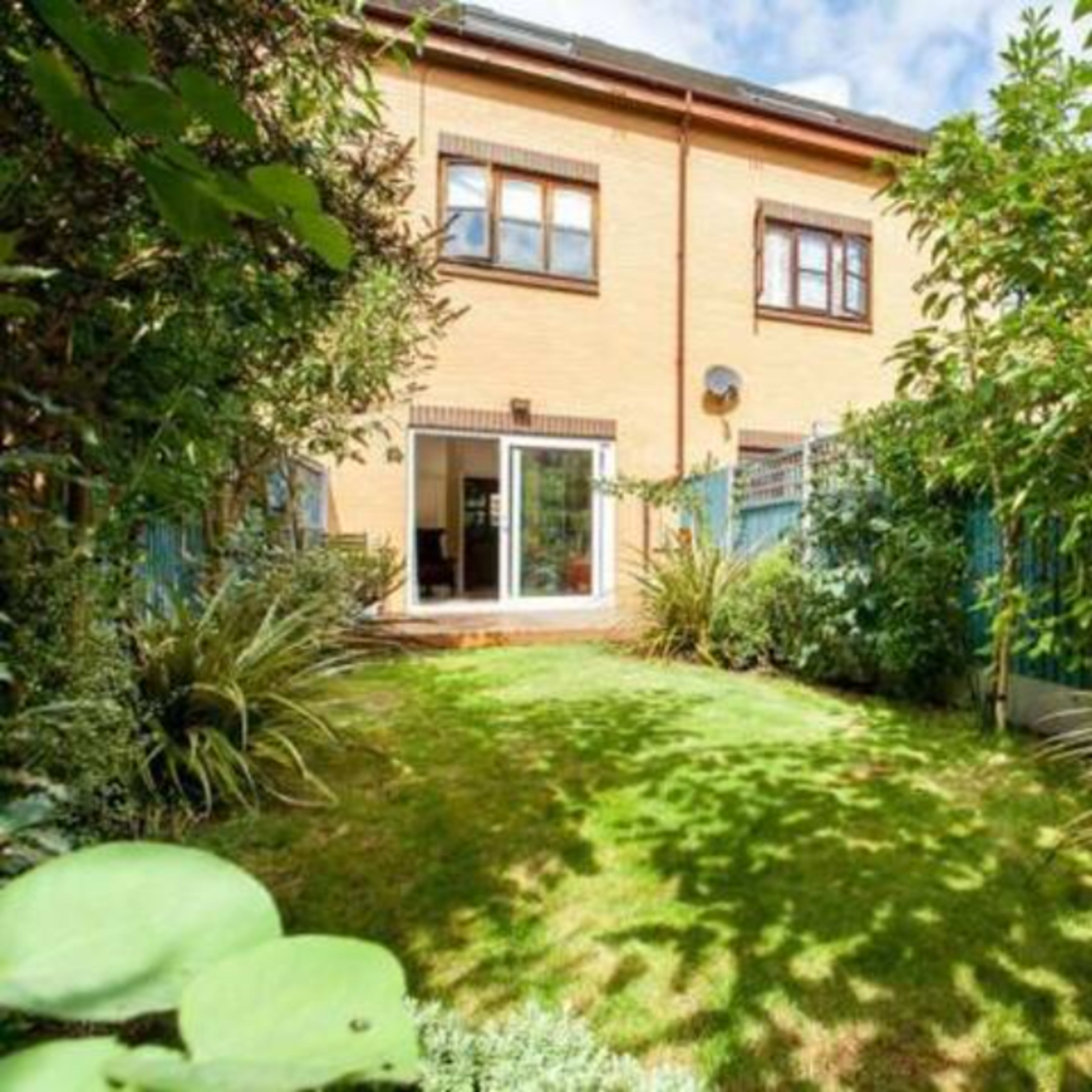 A well-maintained backyard with a neat lawn and surrounding greenery adjacent to a brick building.