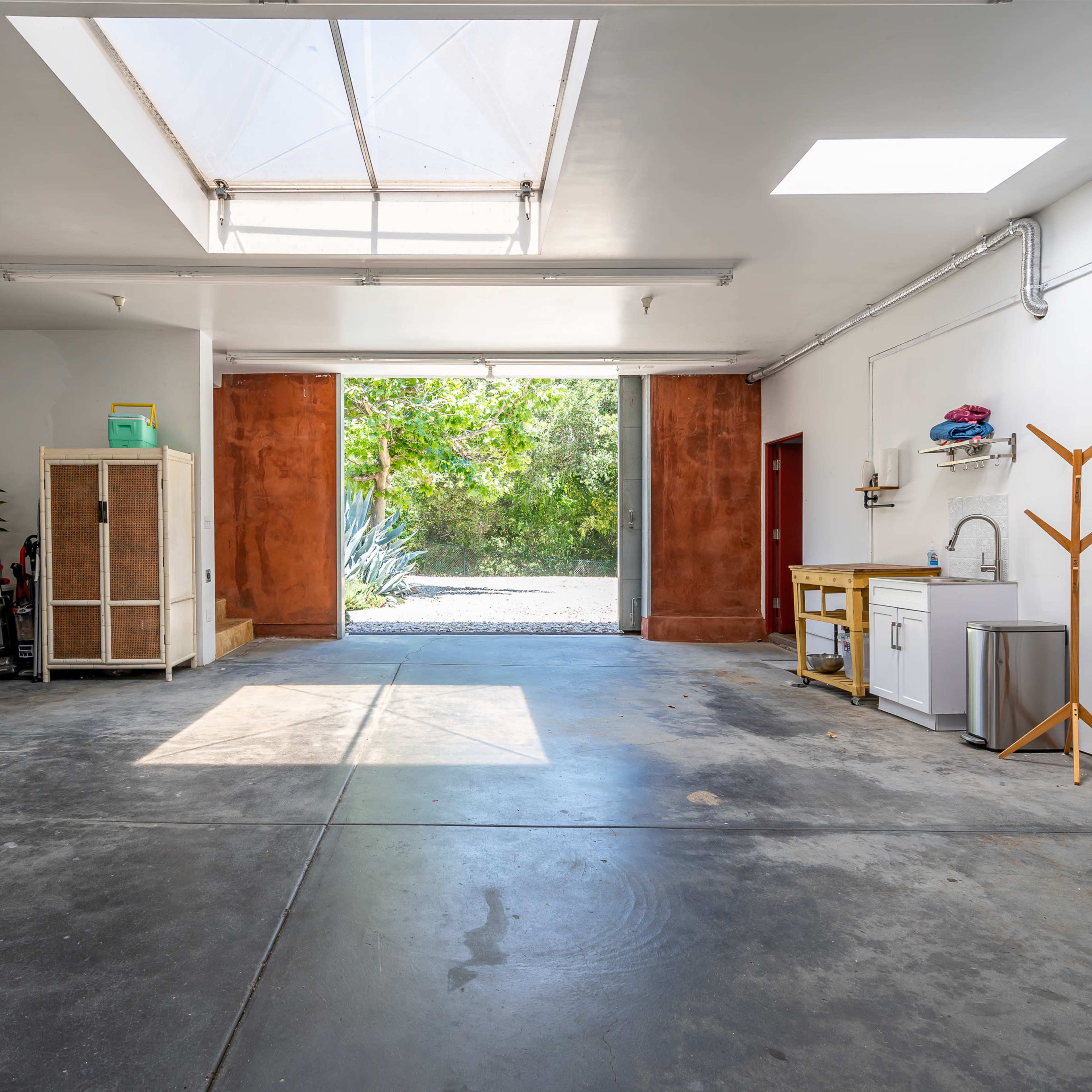 A spacious garage features a skylight, storage cabinets, and a clear view of greenery through an open door.