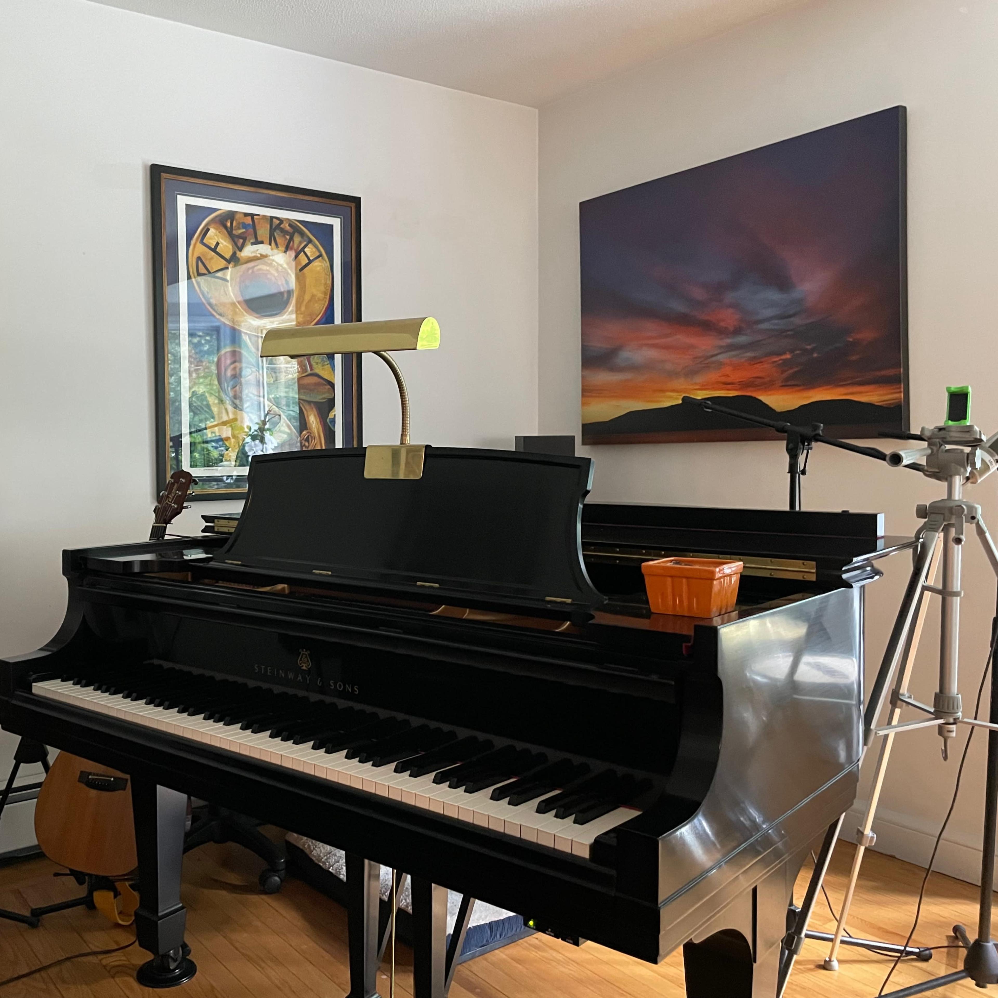 A grand piano sits in a room decorated with framed artwork, alongside various musical instruments and equipment.