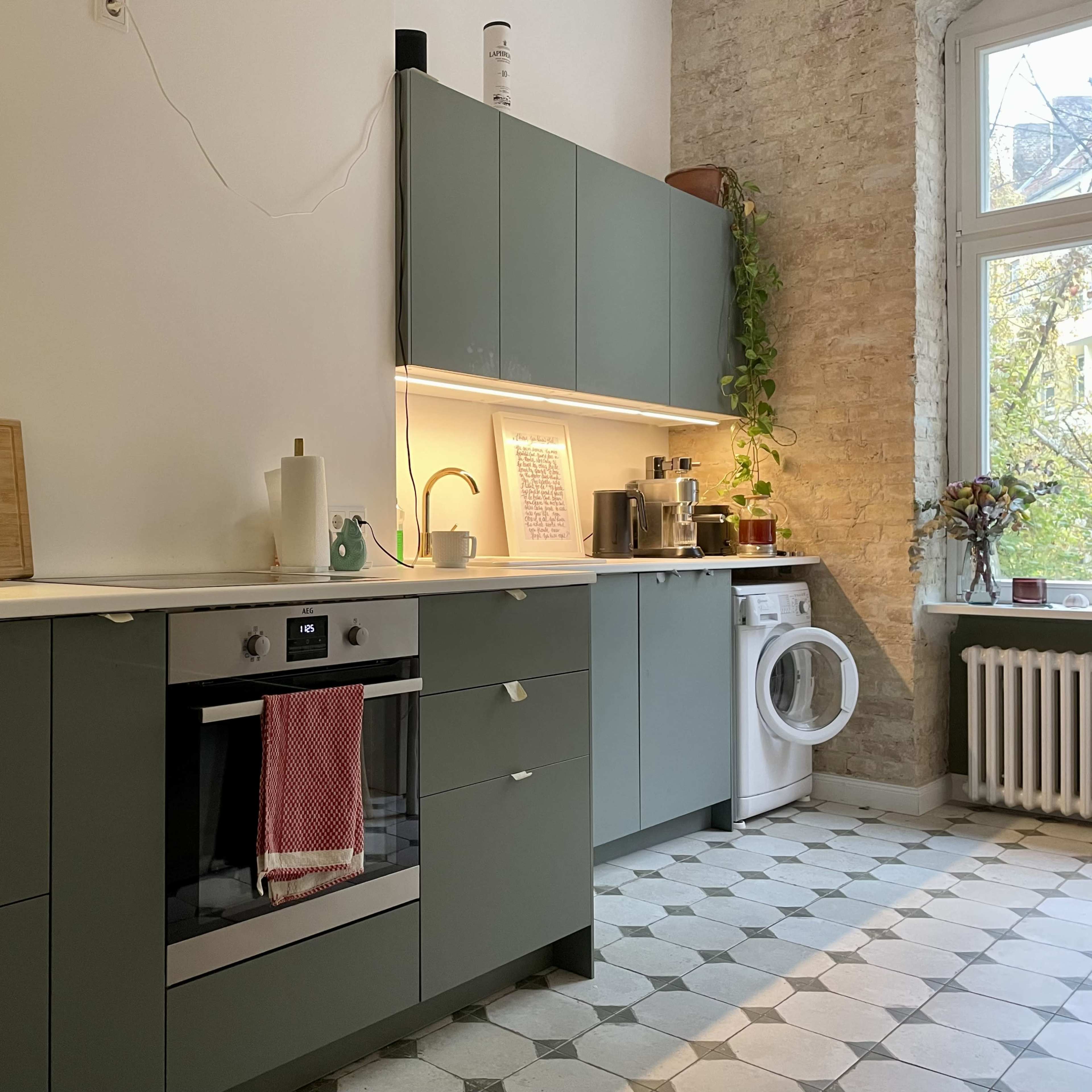 A modern kitchen with green cabinetry, a built-in oven, and a washing machine beside a window.