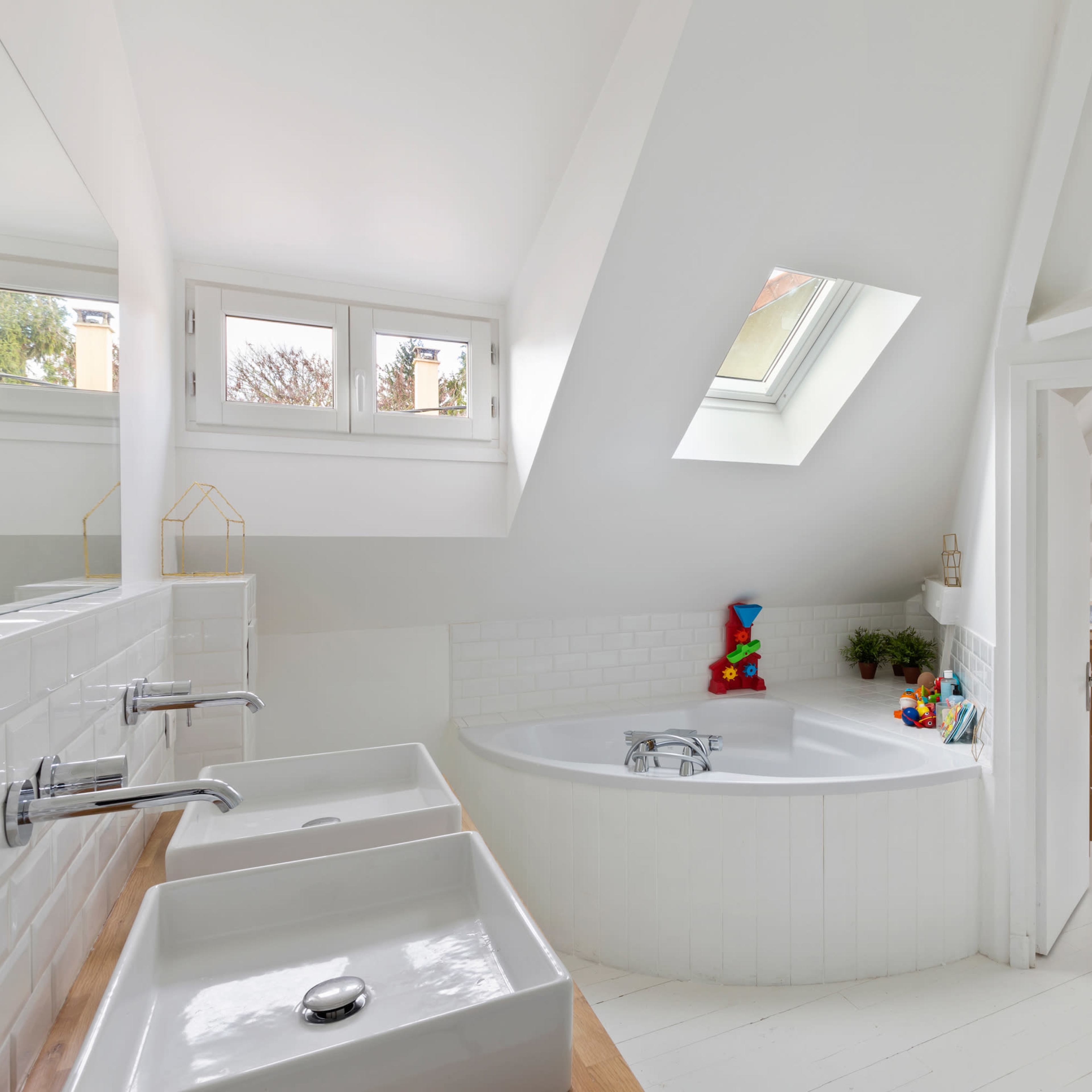 A bright, modern bathroom featuring a spacious bathtub, double sinks, and sloped ceilings with a skylight.