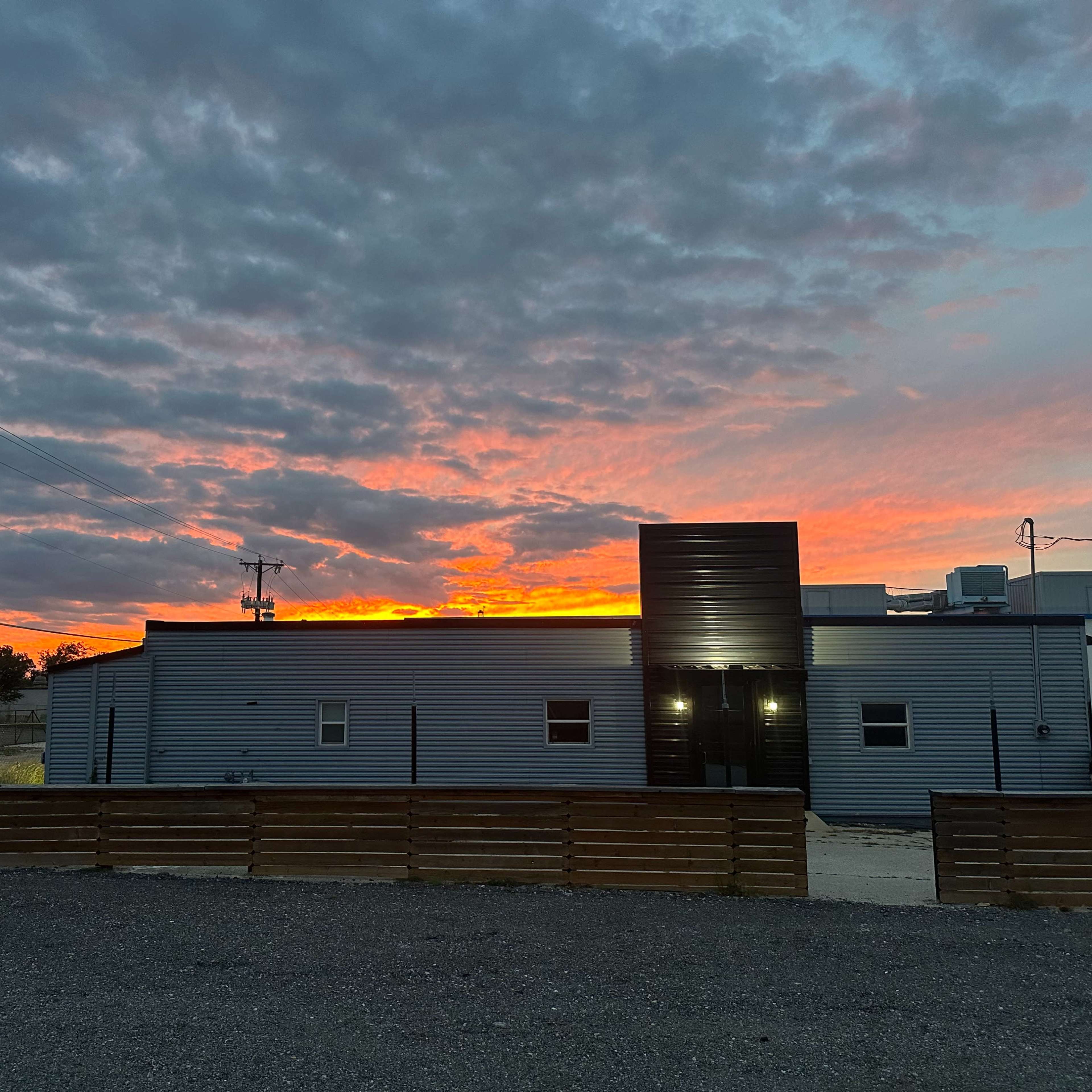 A gray building with a black section stands against a vibrant sunset sky filled with clouds.
