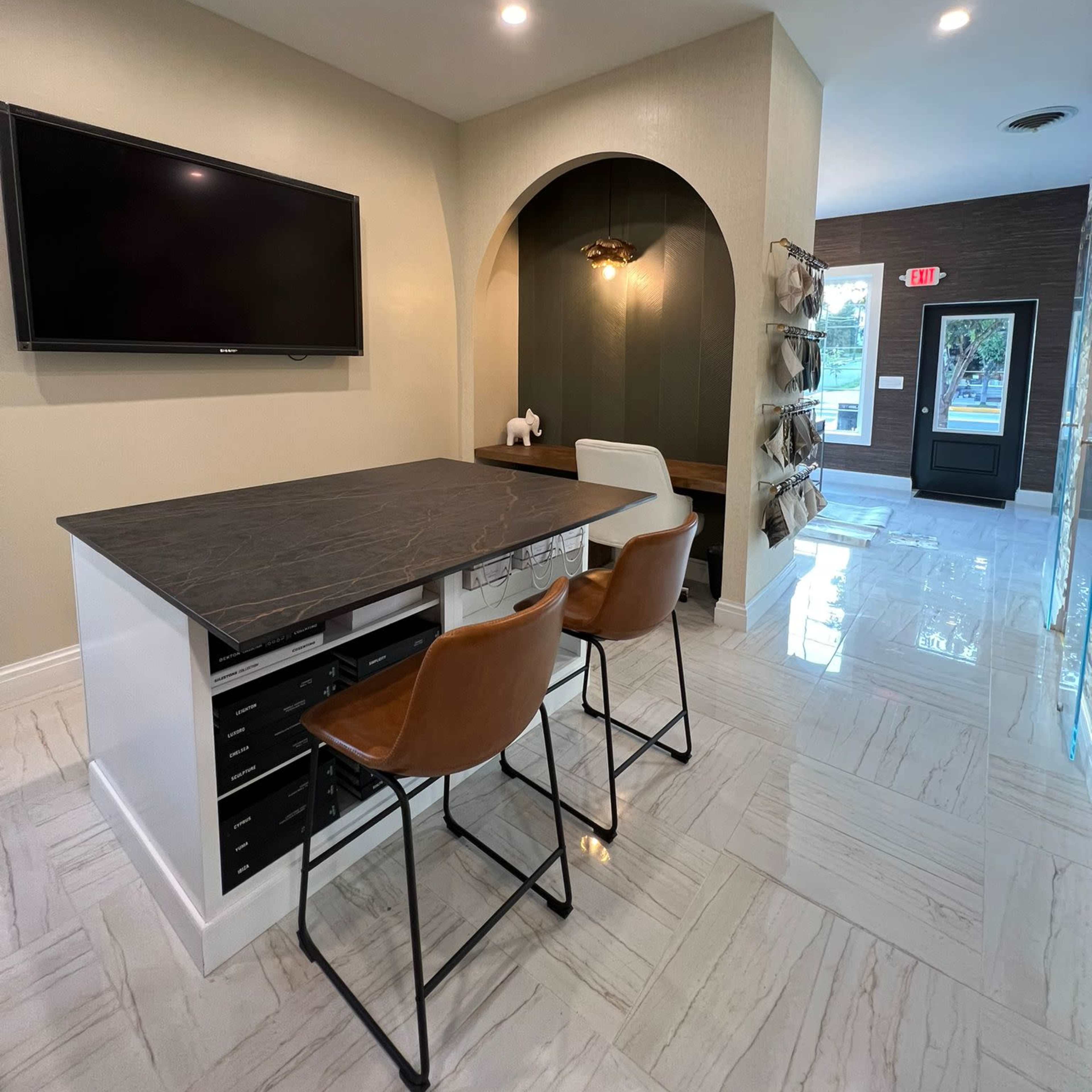 A modern office space with a desk and two chairs, a television mounted on the wall, and a large arched alcove.
