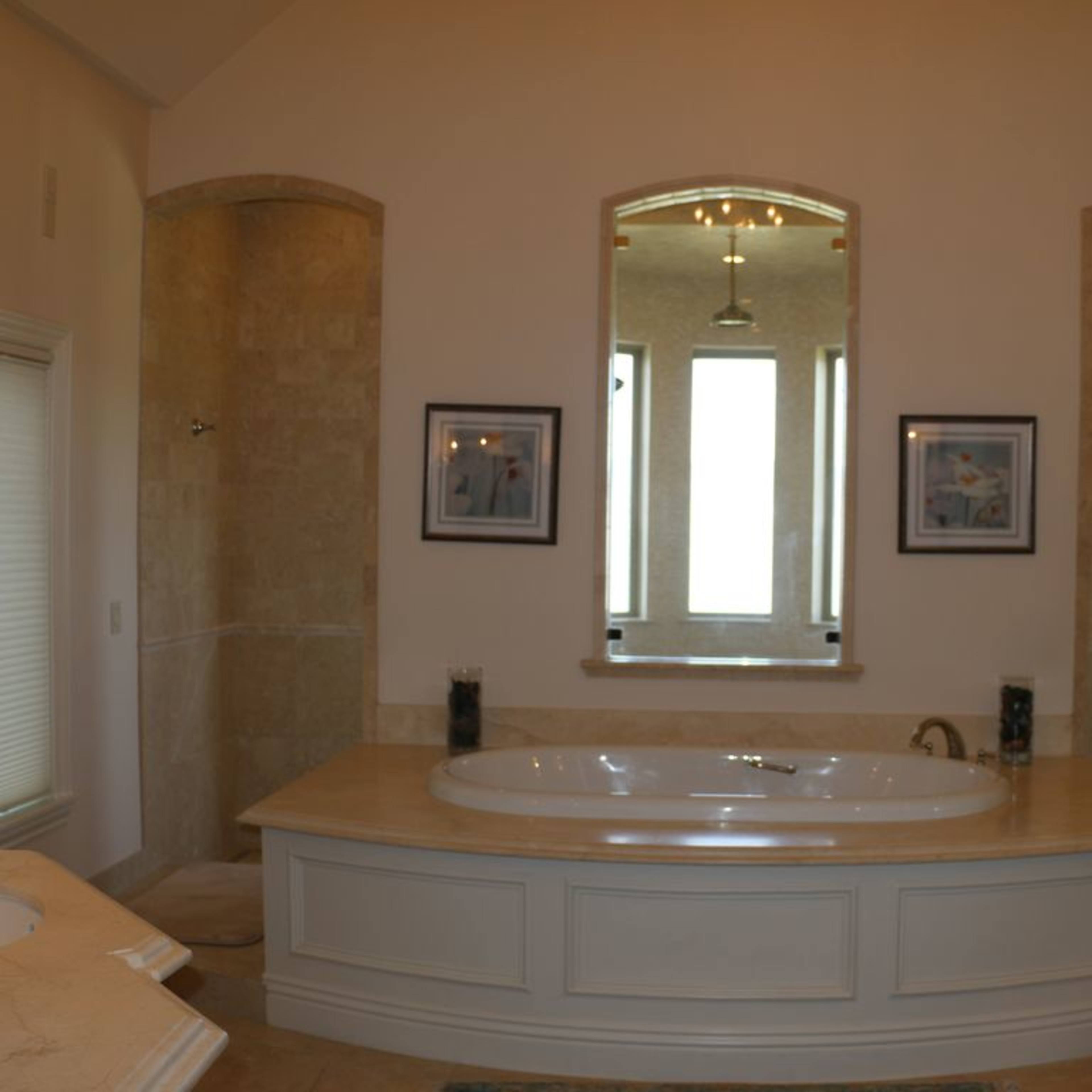 A spacious bathroom with a large bathtub, dual sinks, and natural light coming through three windows.
