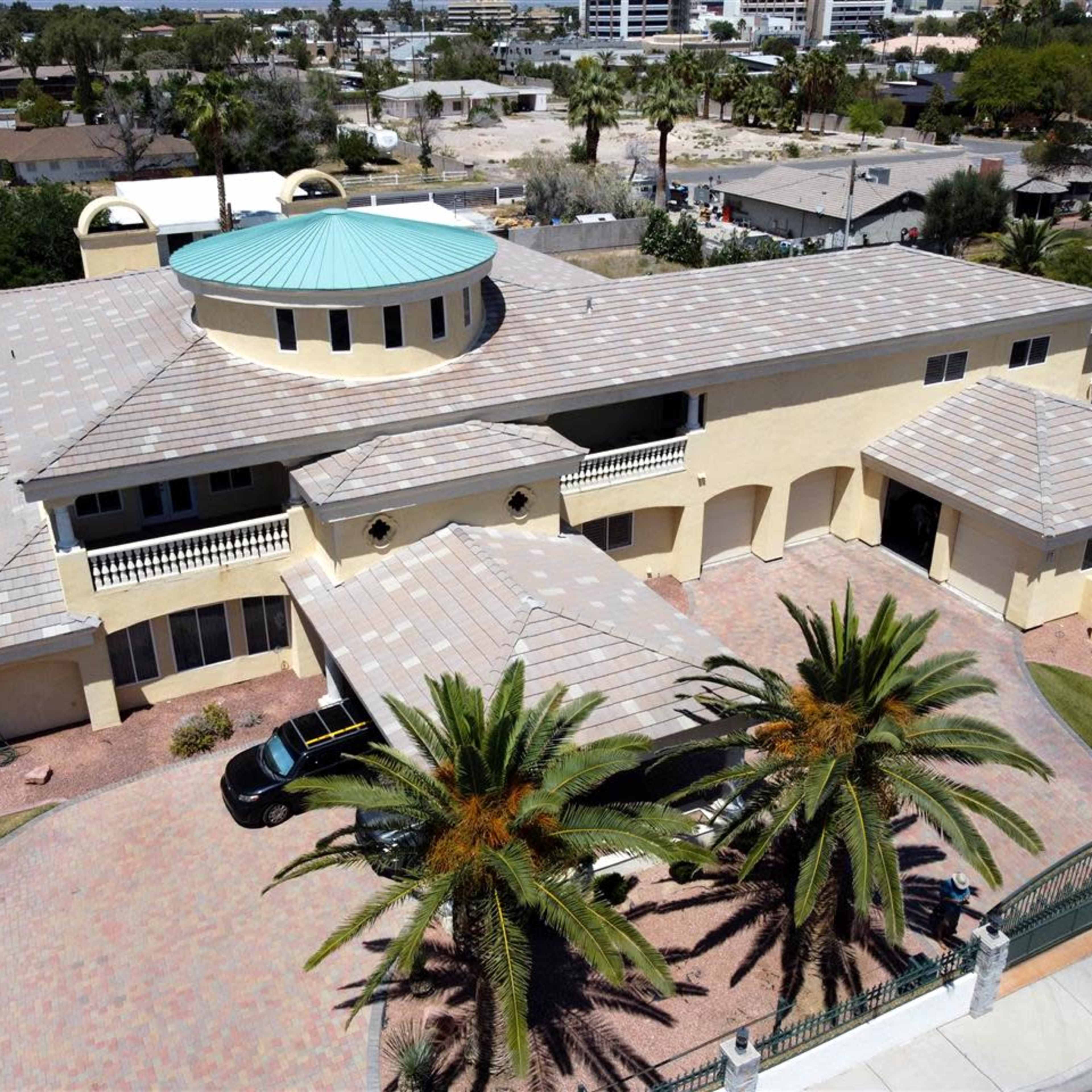 A large, two-story house with a circular roof section and palm trees in the landscaped front yard.
