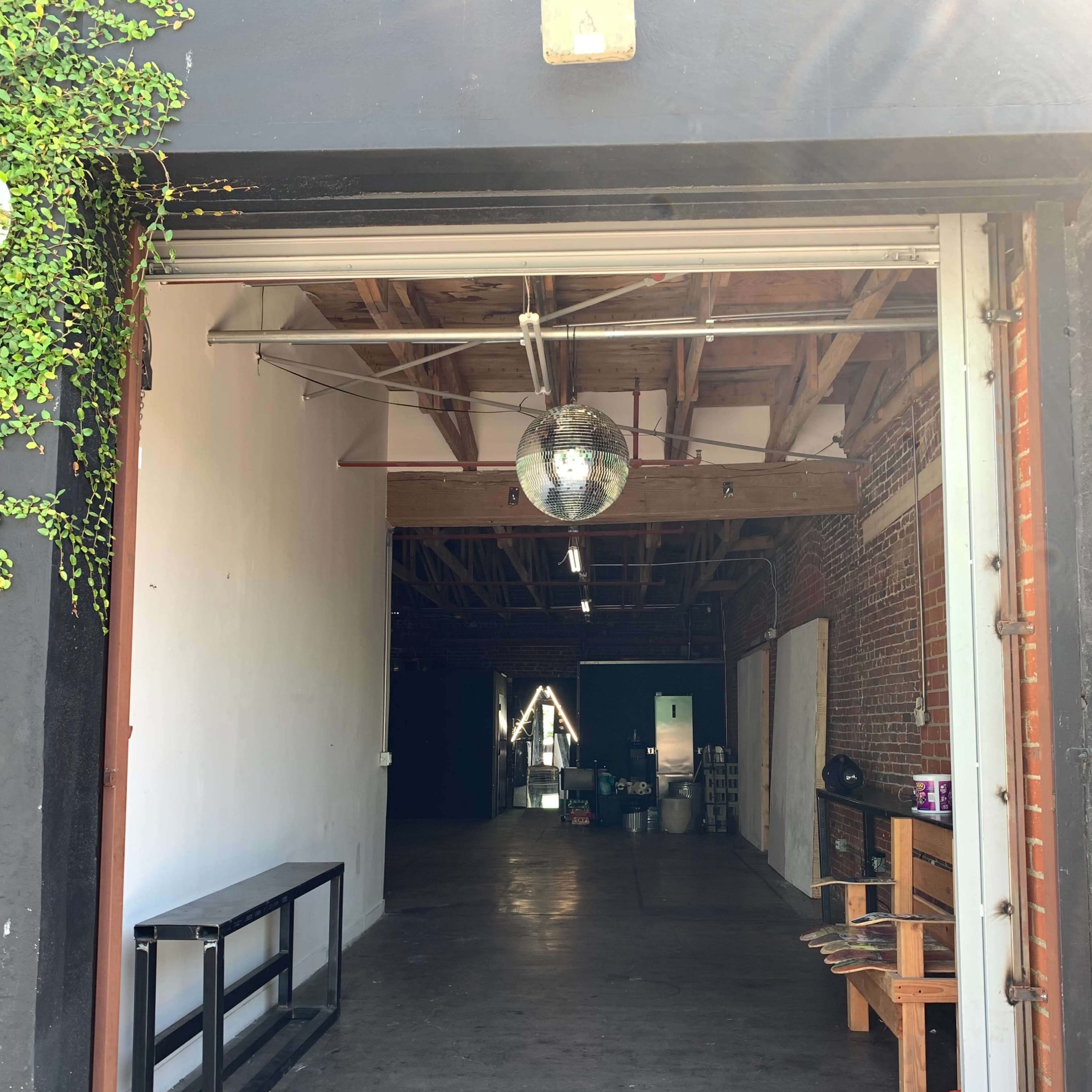 An open doorway leading into a spacious, industrial-style interior with exposed brick walls and a discoball hanging from the ceiling.