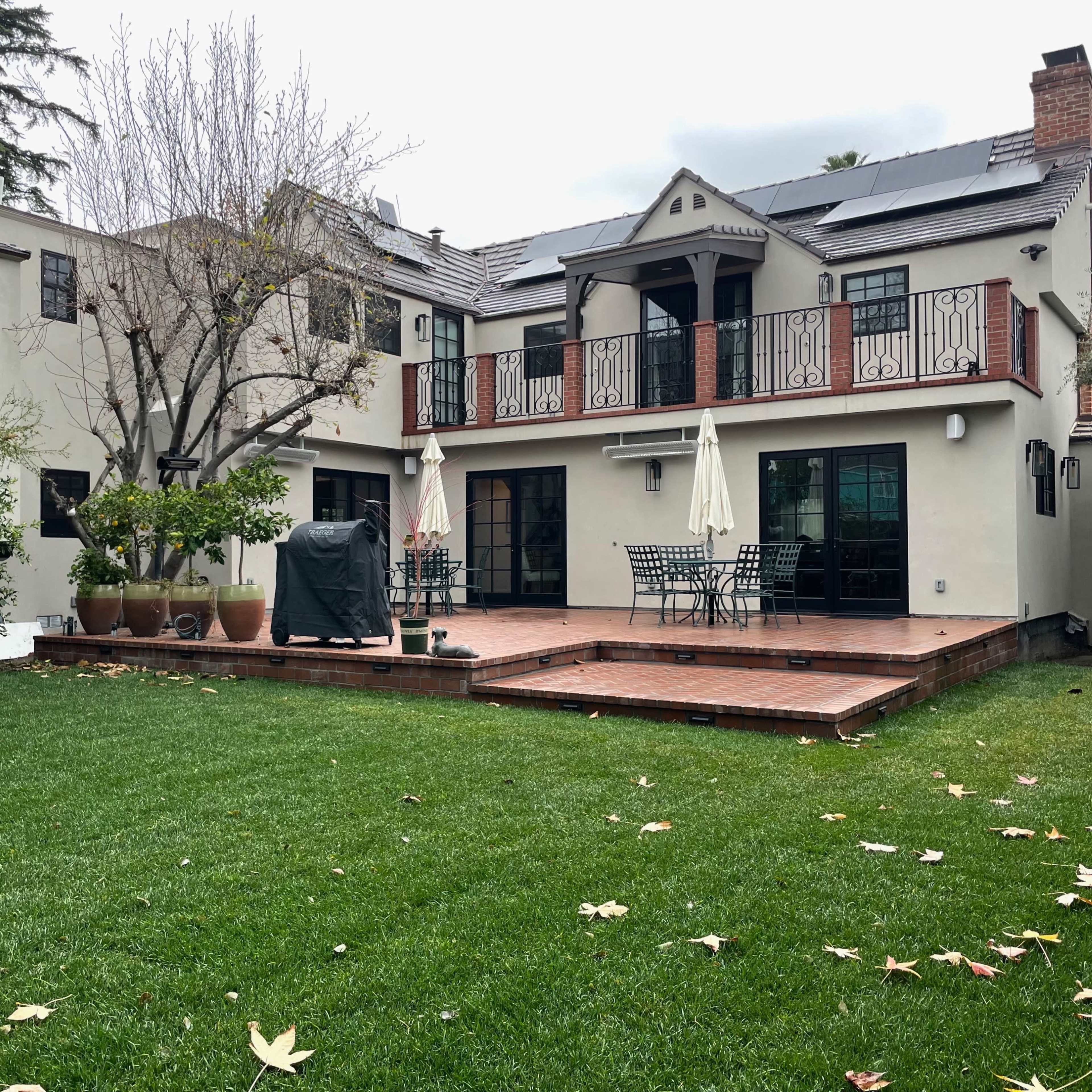 A backyard with a green lawn, a wooden deck with dining furniture, and an adjacent house featuring large windows and a balcony.