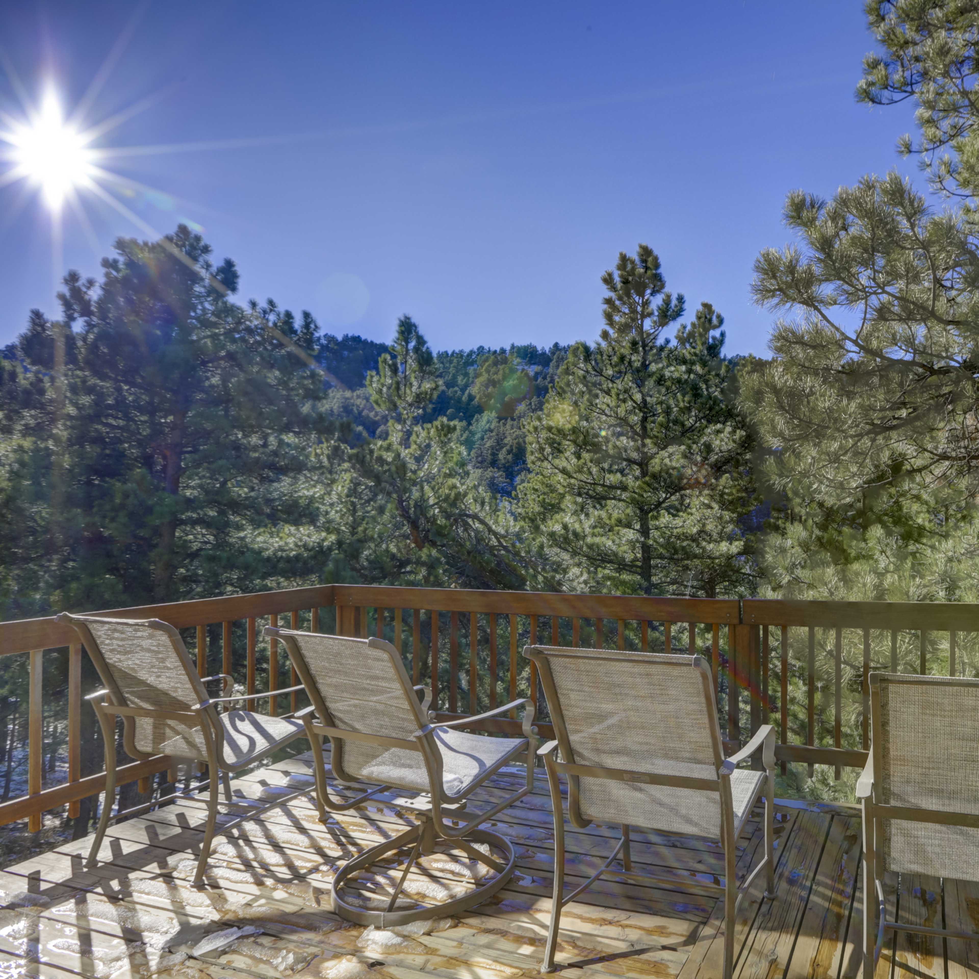 A deck with several chairs overlooks a forested area under a clear blue sky.