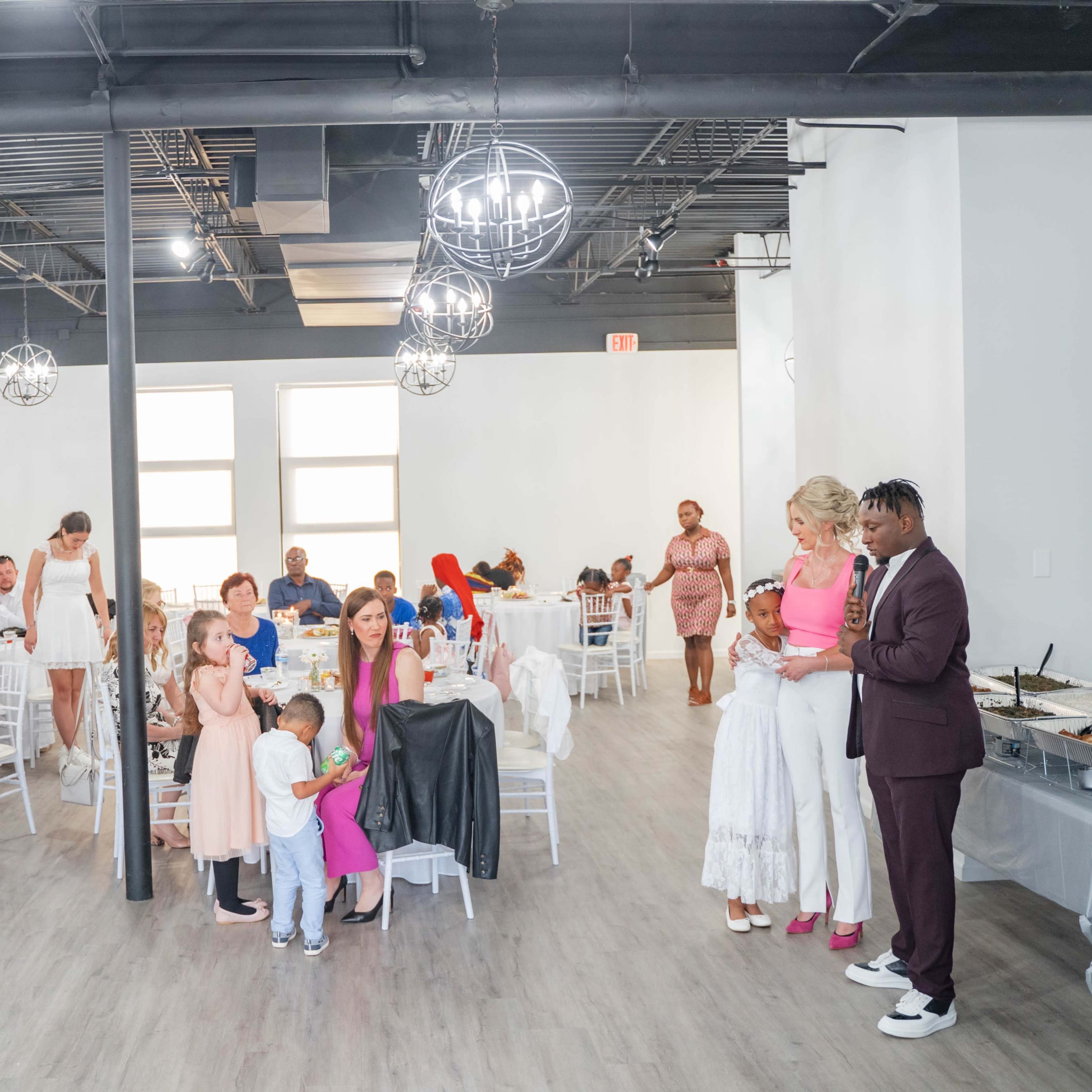 A diverse group of people gathers at a reception in a spacious, well-lit venue with white walls and modern decor.