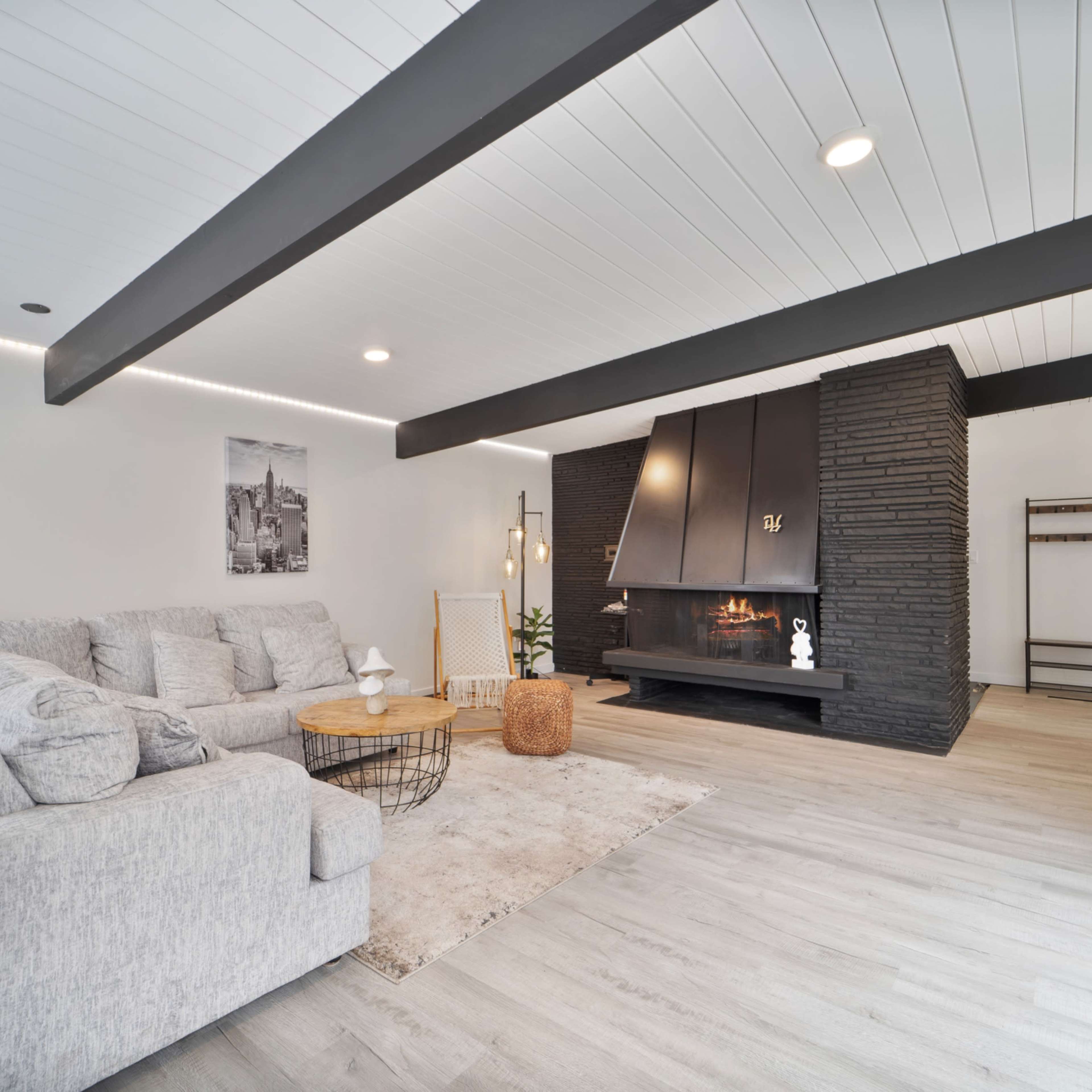 A modern living room with a gray sectional sofa, a round wooden coffee table, and a black stone fireplace against a white wall.