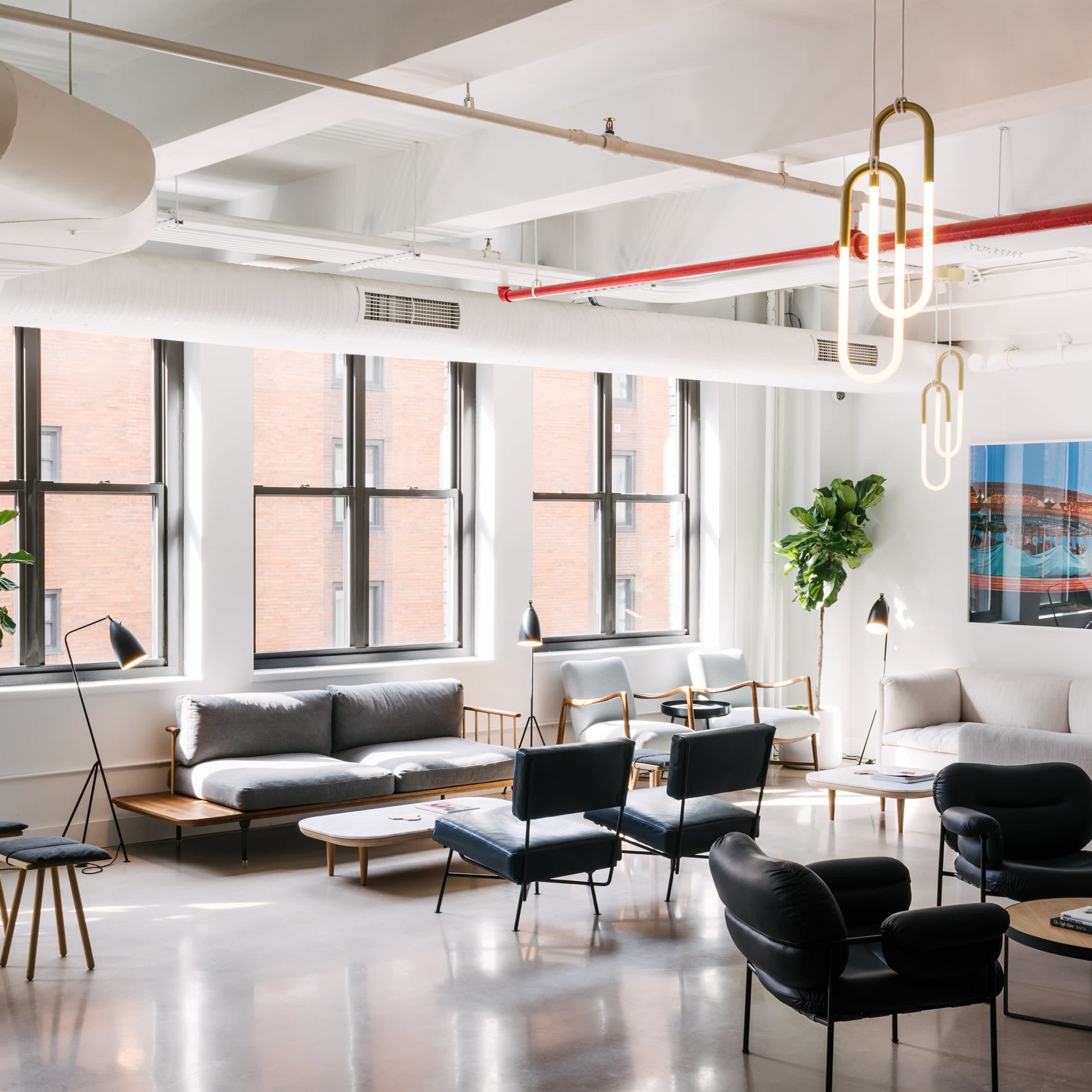 A modern coworking space featuring sleek furniture, plants, and large windows that allow natural light to fill the room.