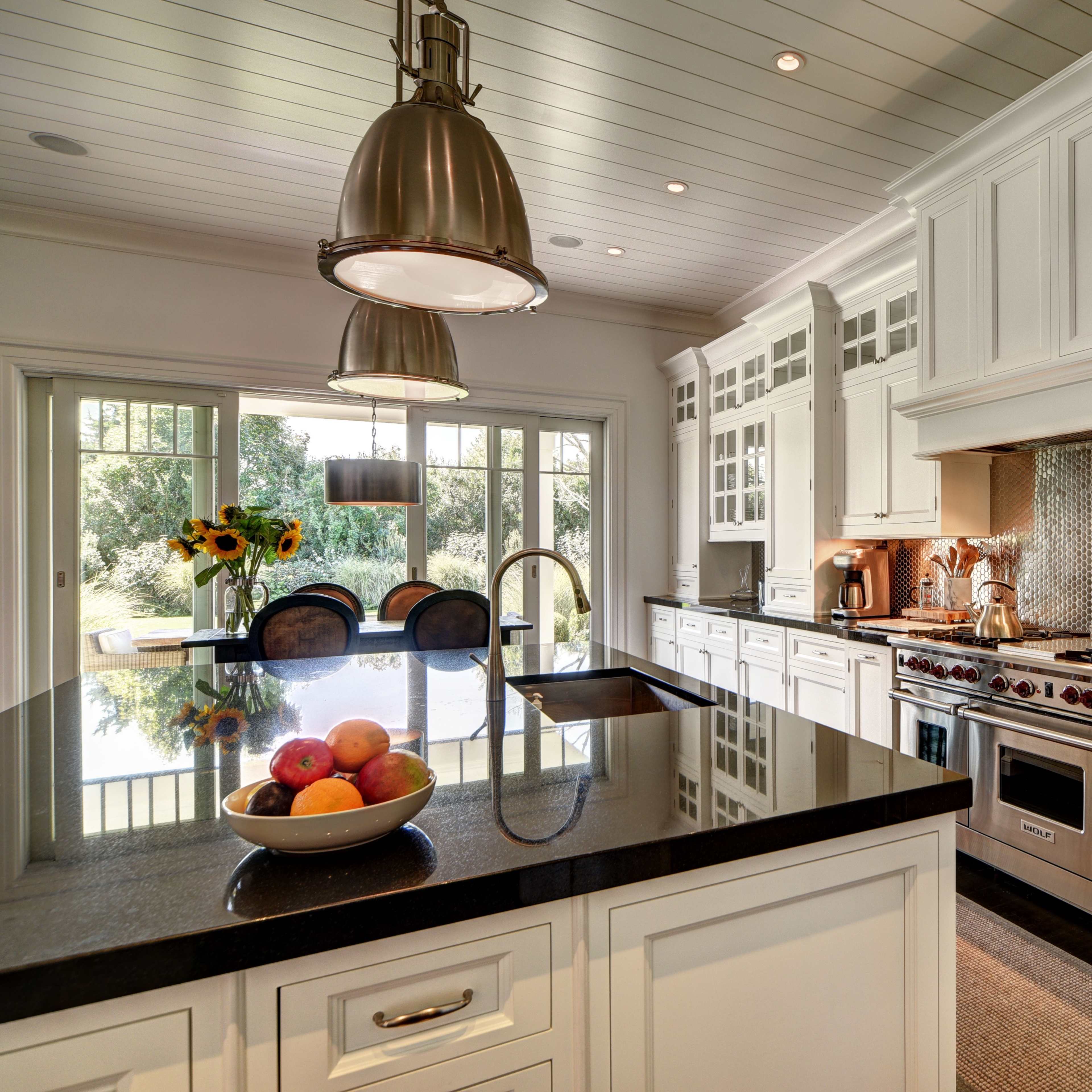 A modern kitchen with white cabinetry, a dark countertop, stainless steel appliances, and a bowl of fruit on the island.