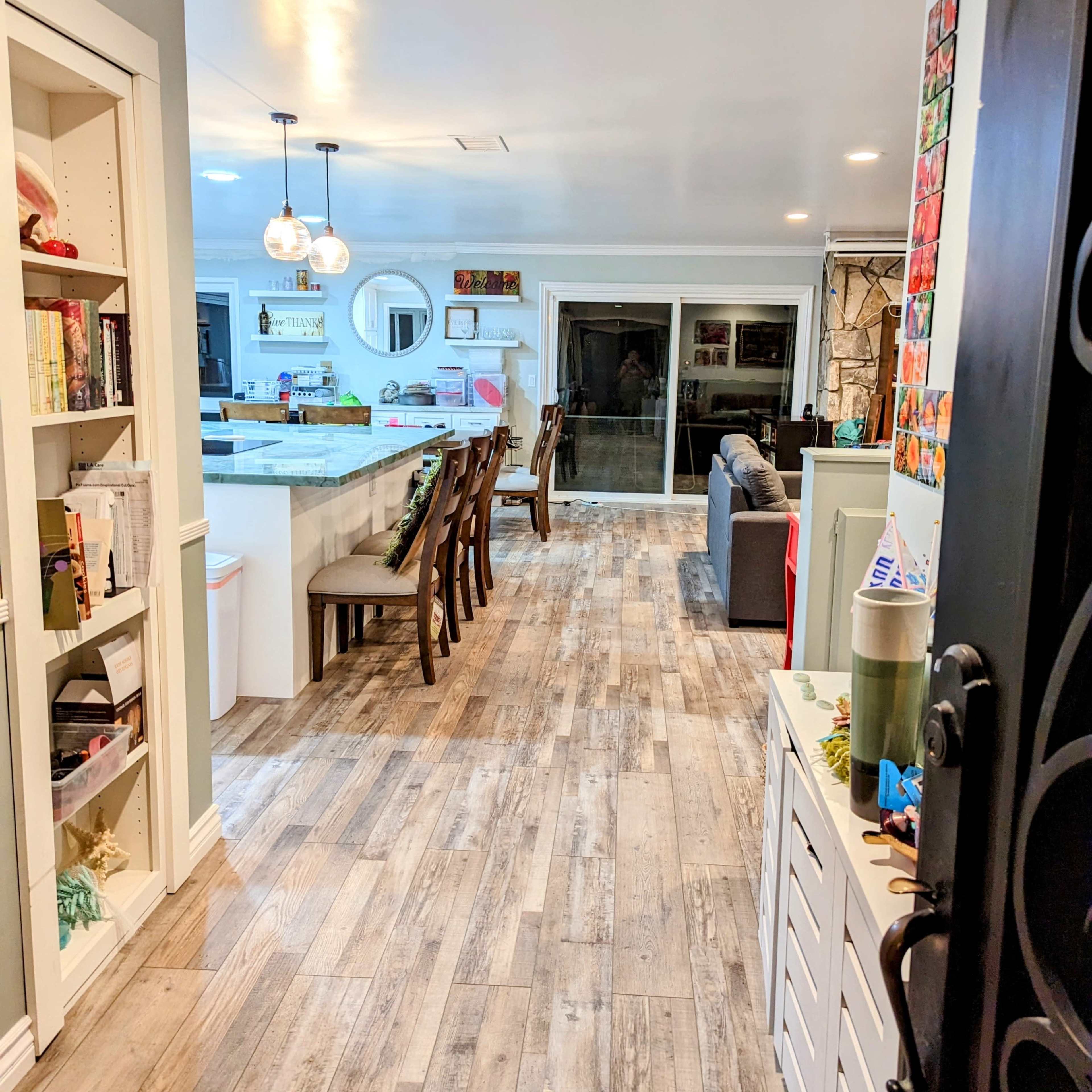 A well-lit hallway leads to an open kitchen and living area, featuring wooden flooring and a combination of bookshelves and seating.