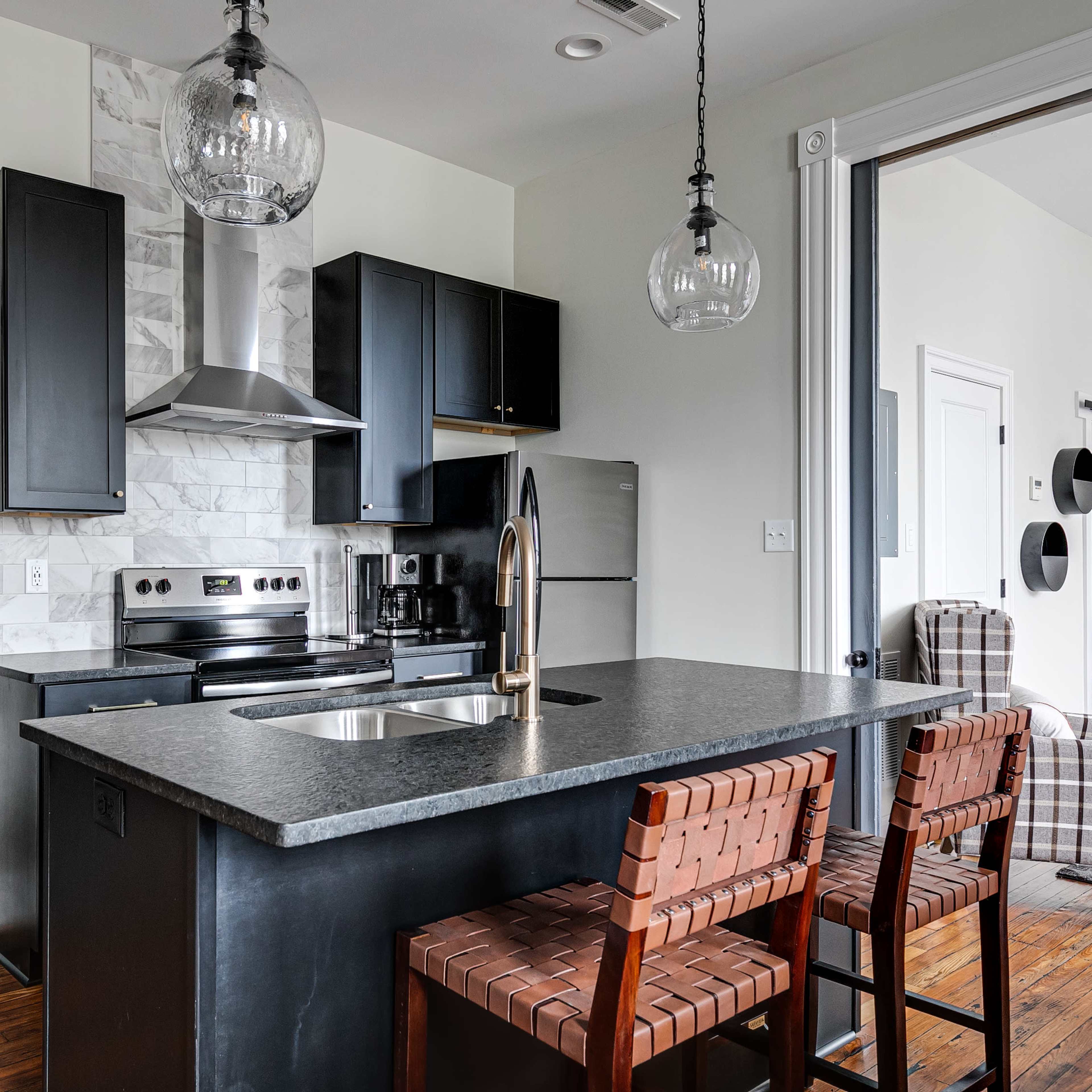 A modern kitchen featuring a black countertop, stainless steel appliances, and two wooden bar stools.