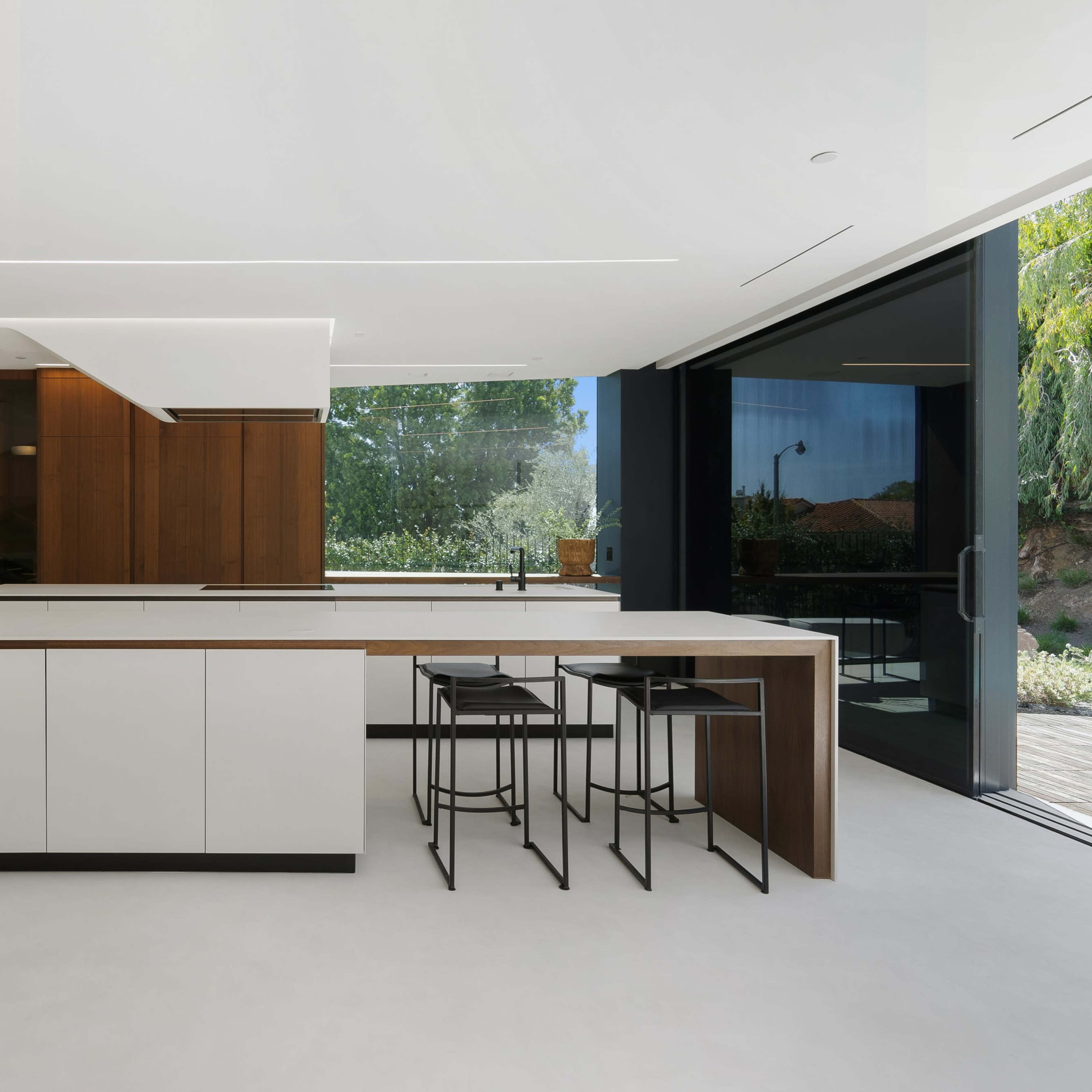 A modern kitchen with a central island, sleek cabinetry, and large windows overlooking a landscaped outdoor area.