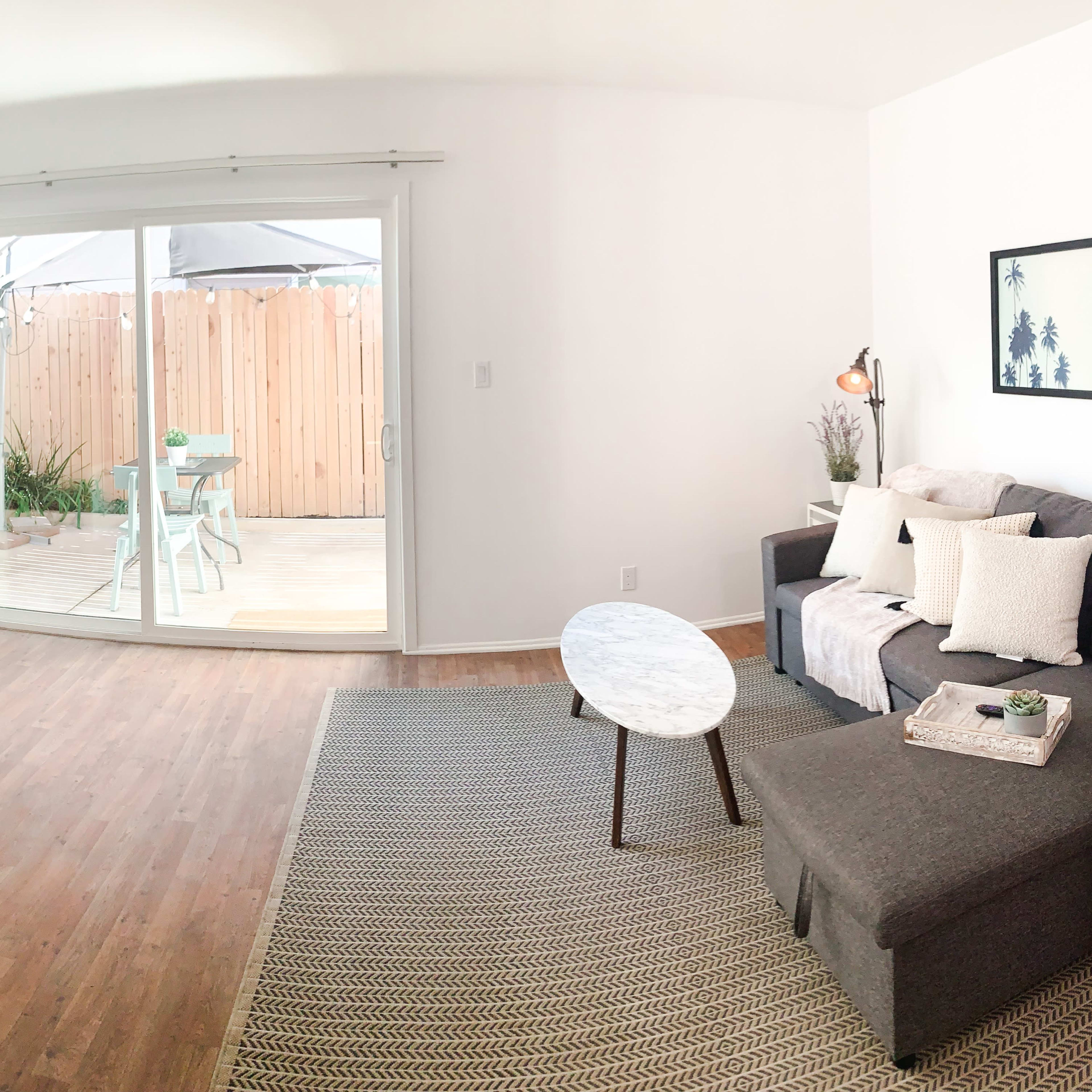 A modern living room with a gray sectional sofa, a round marble coffee table, a television on a wooden stand, and large sliding doors that open to a deck area.