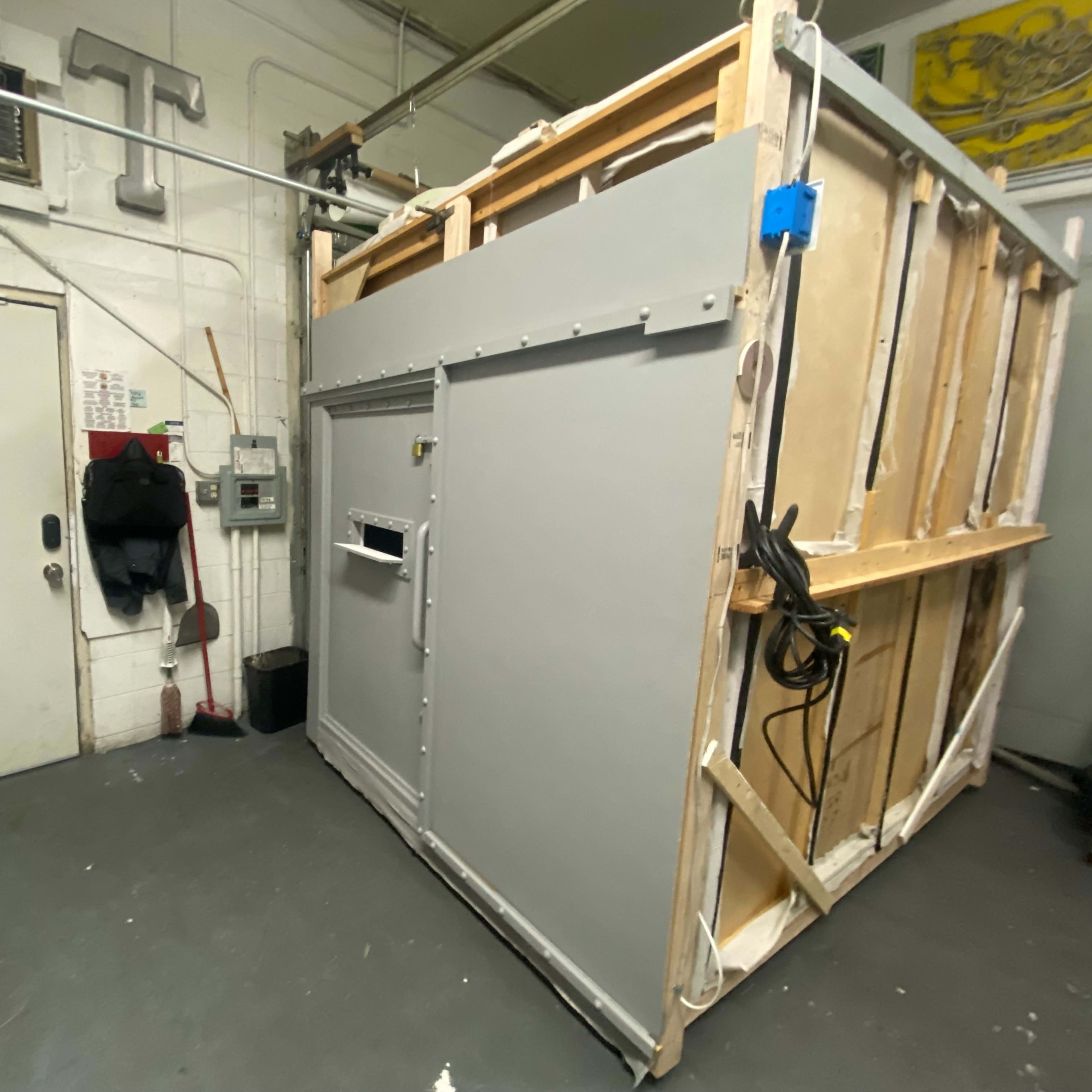 A large, gray structure with a door and an attached ventilation system located in a dimly lit room.